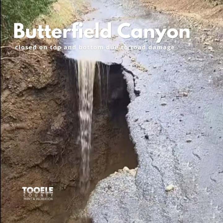 Large washout hole in a dirt road with water flowing into the gap.