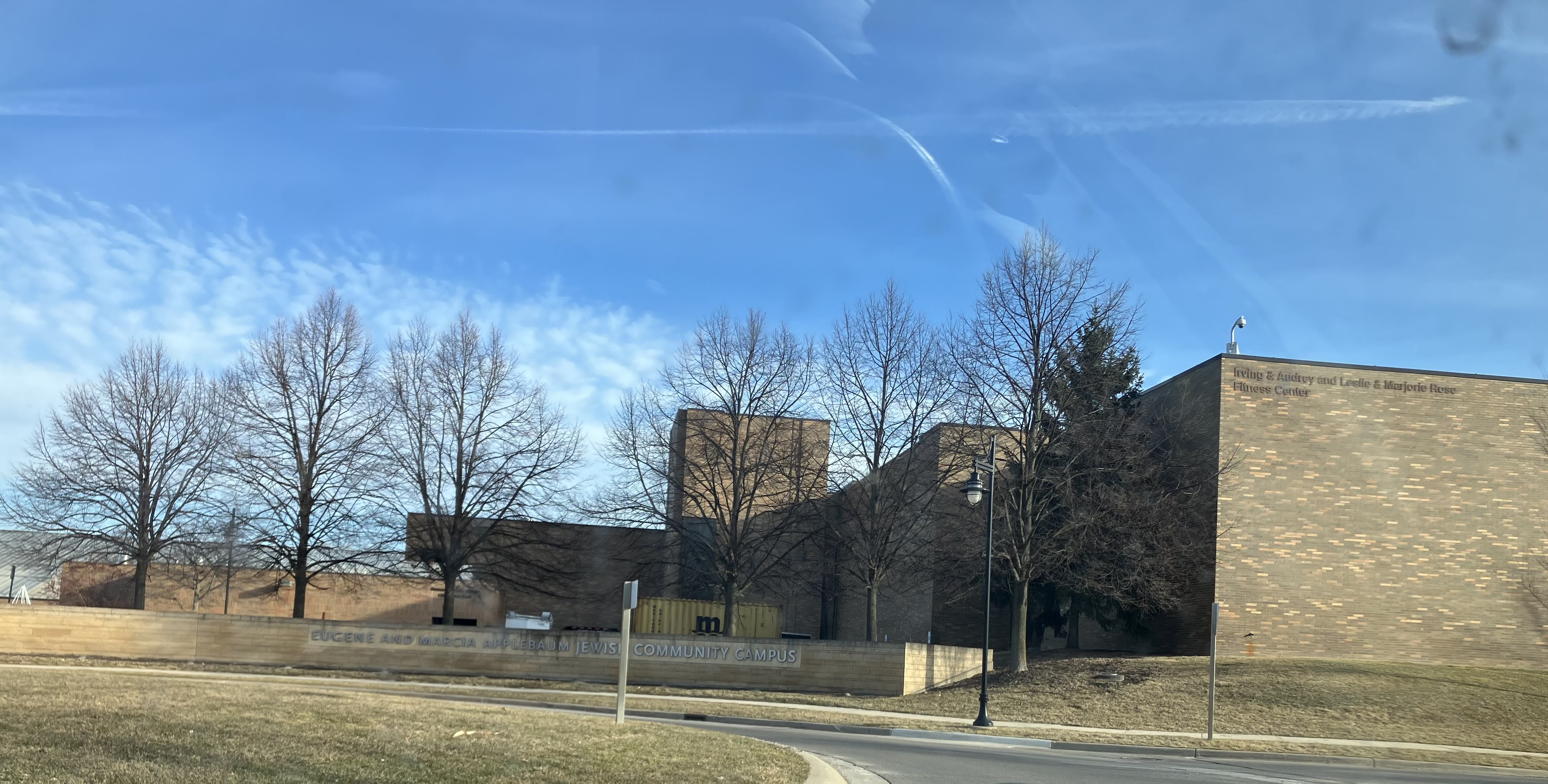 Multi-section brick building with bare trees and a parking lot in front.