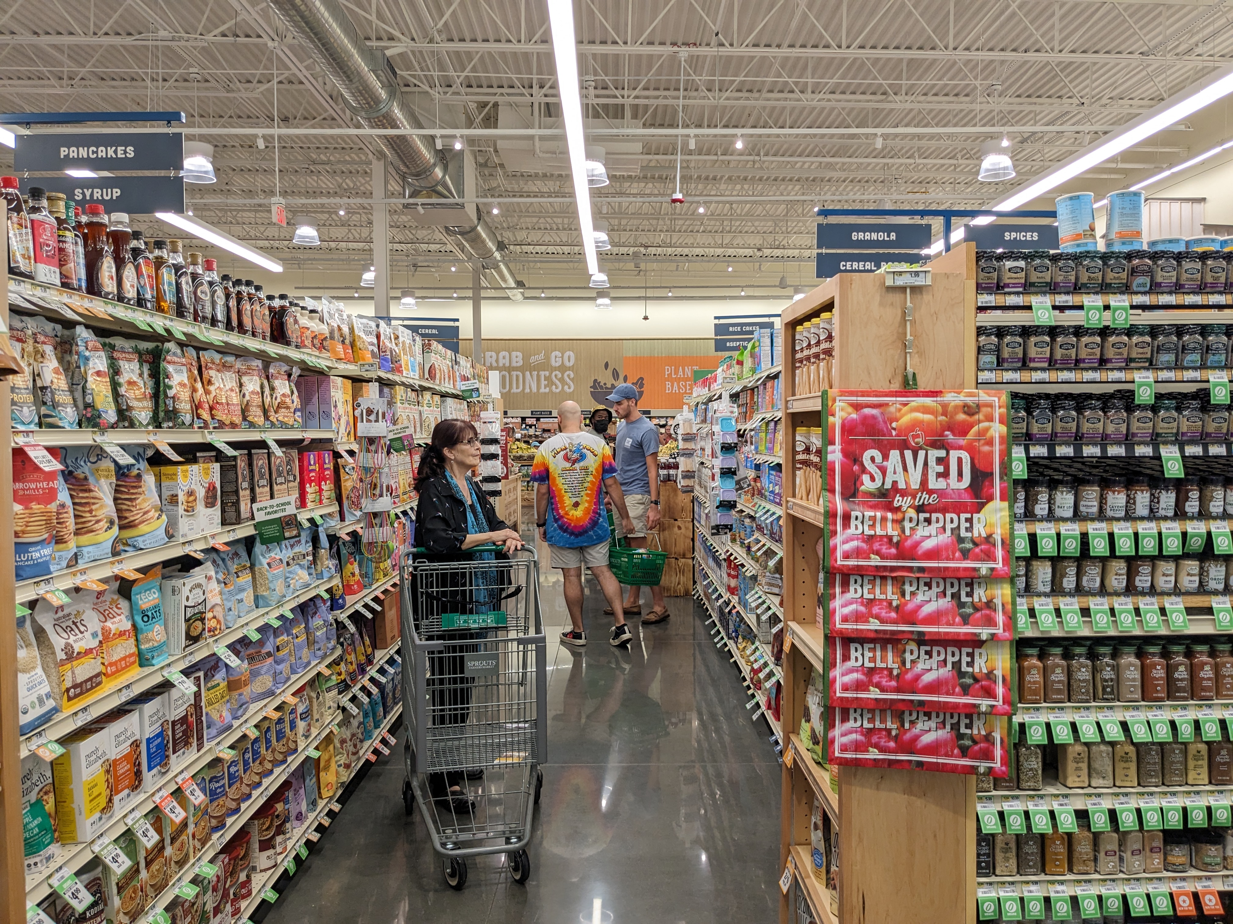Shopper pushing a cart down a well-stocked grocery aisle inside a Sprouts Farmers Market.