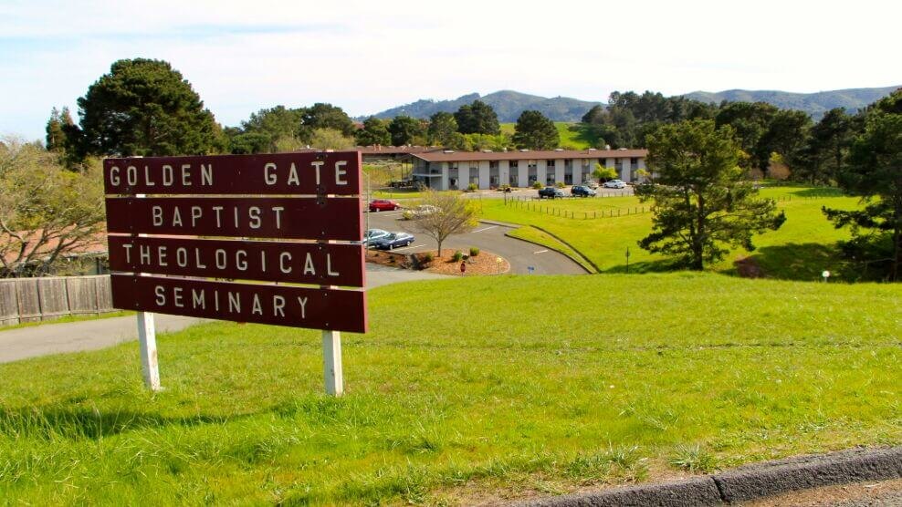 Wooden sign for Golden Gate Baptist Theological Seminary in front of a green hillside campus.