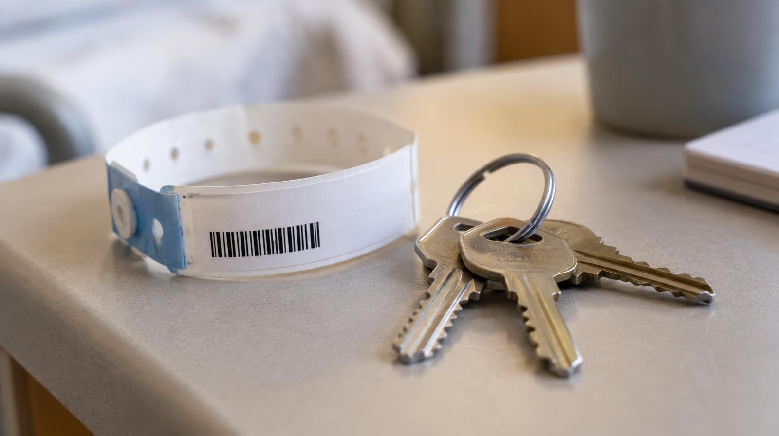A hospital wristband and a set of house keys resting on a plain surface.