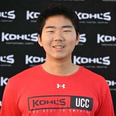 Young male athlete in a red Kohl's UCC shirt poses in front of a branded backdrop.