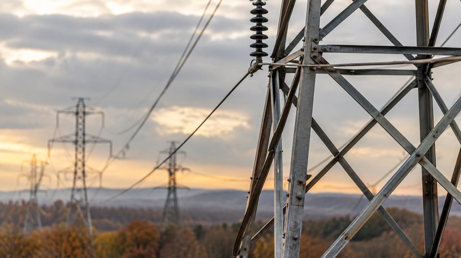 Steel electrical transmission towers with power lines under an overcast sky.