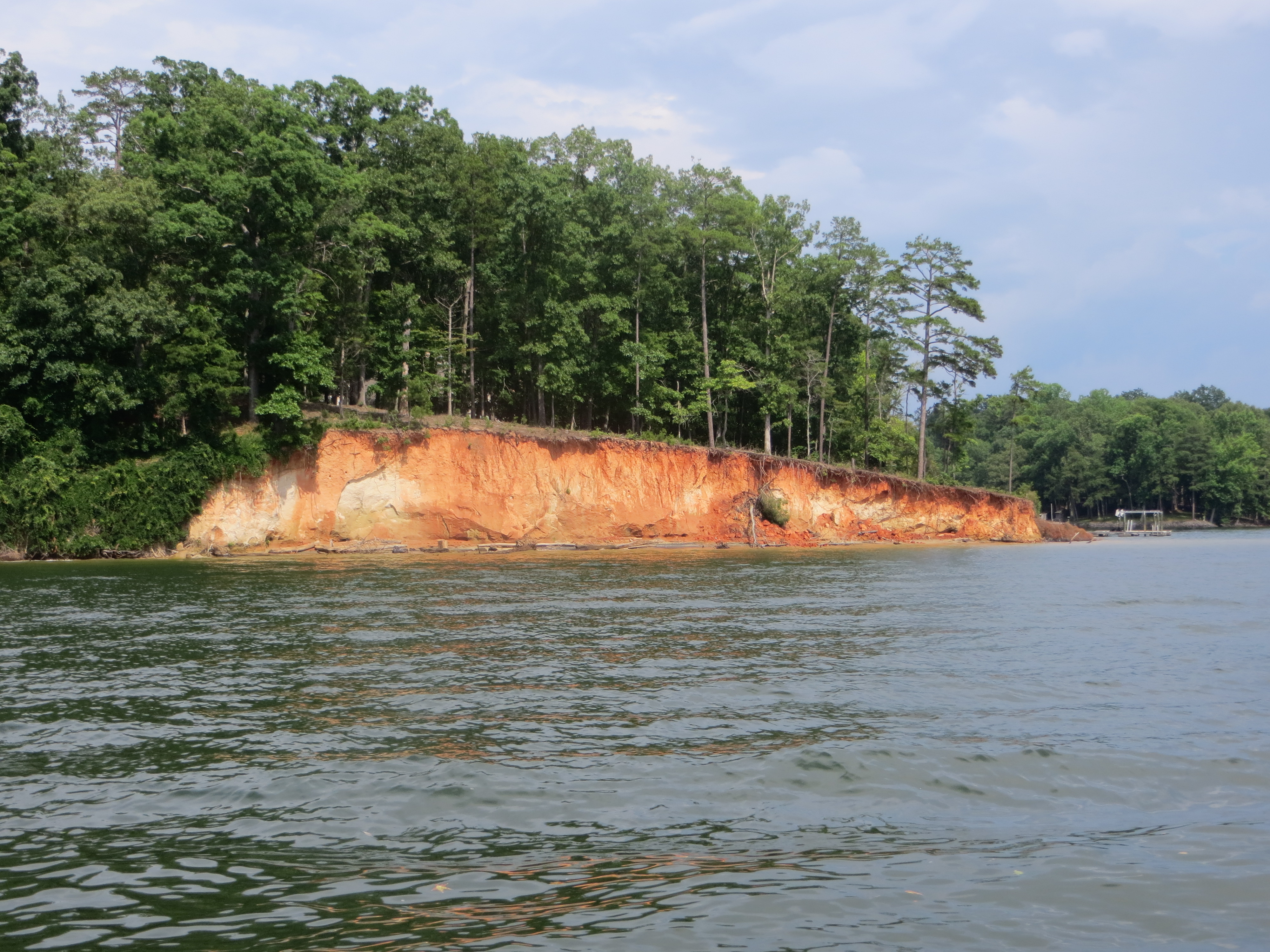 Lake shoreline with wide band of exposed red clay banks and calm water.