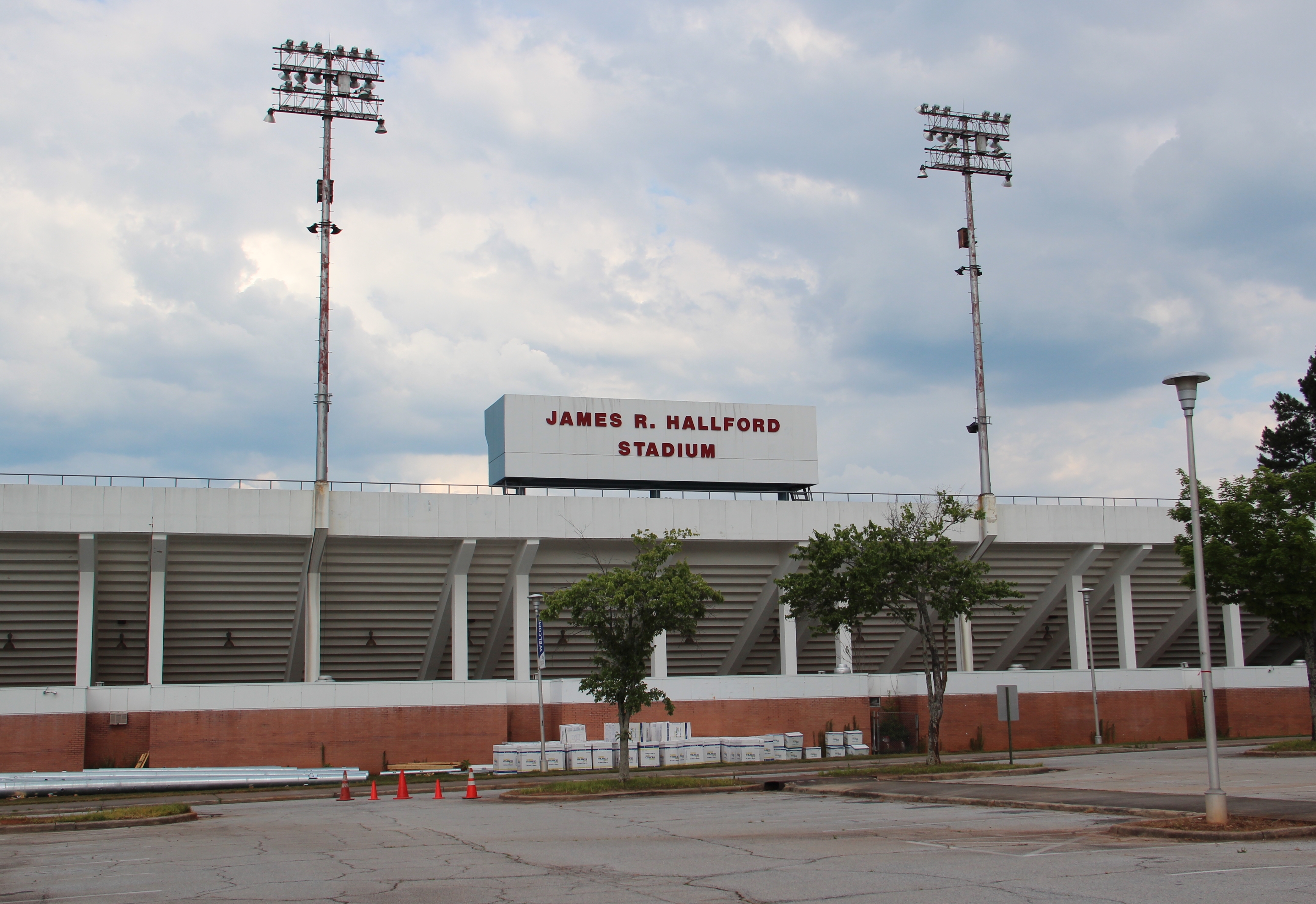 Exterior of a stadium with tall light towers, red and white facade, and a large parking lot.