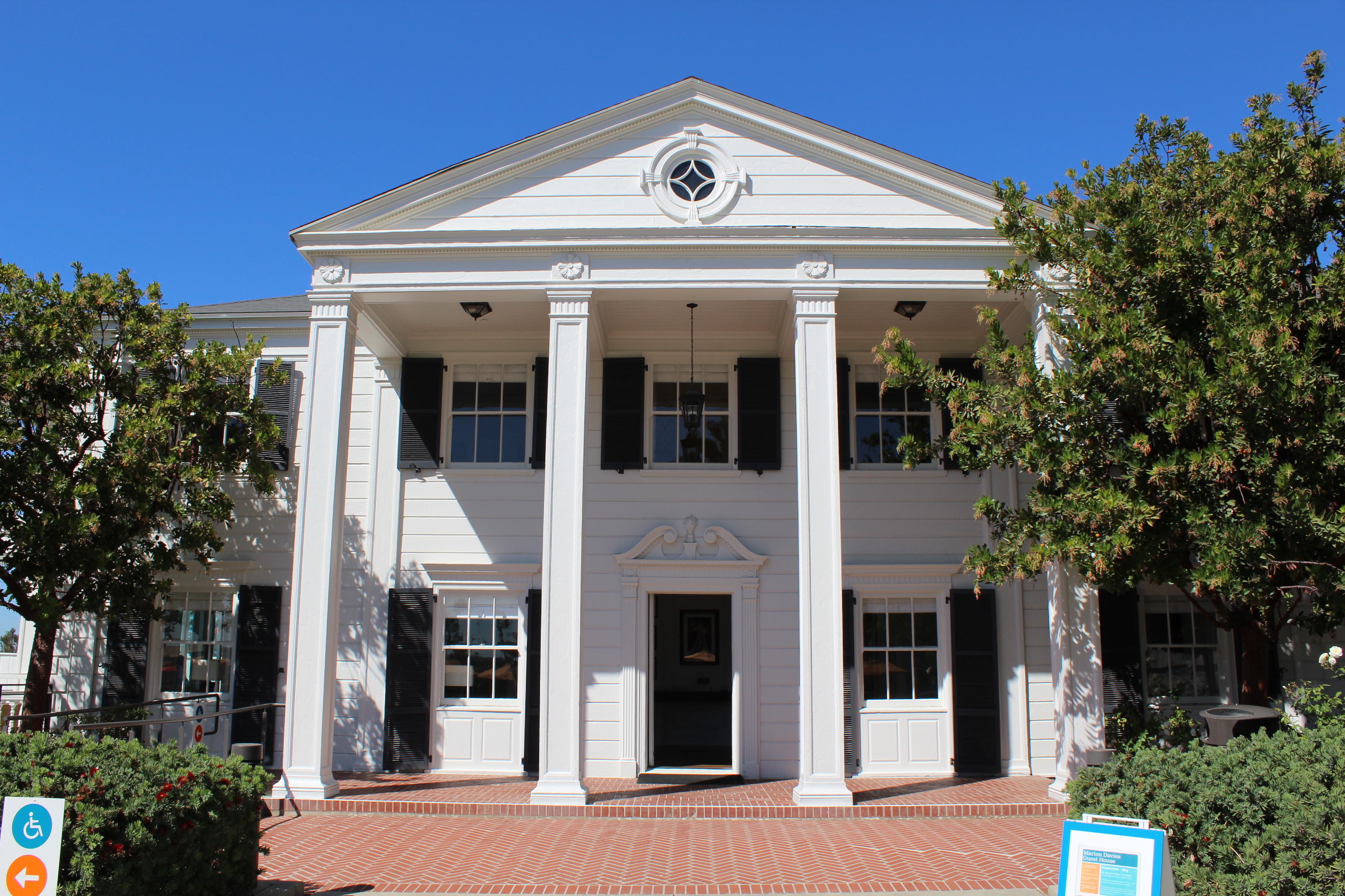 White neoclassical building with tall columns and a triangular pediment surrounded by trees