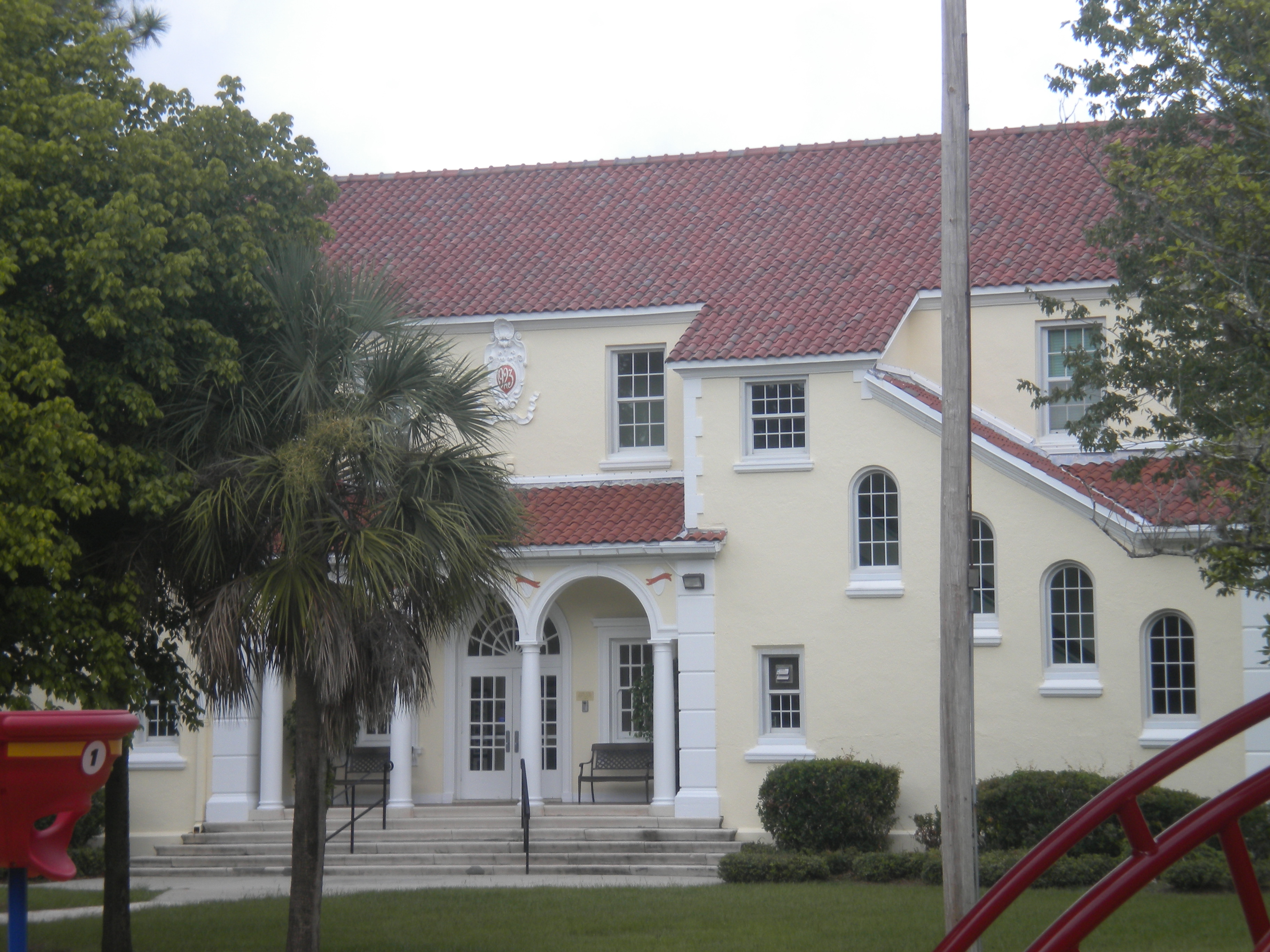 Two-story yellow stucco elementary school building with red tile roof and palm tree.