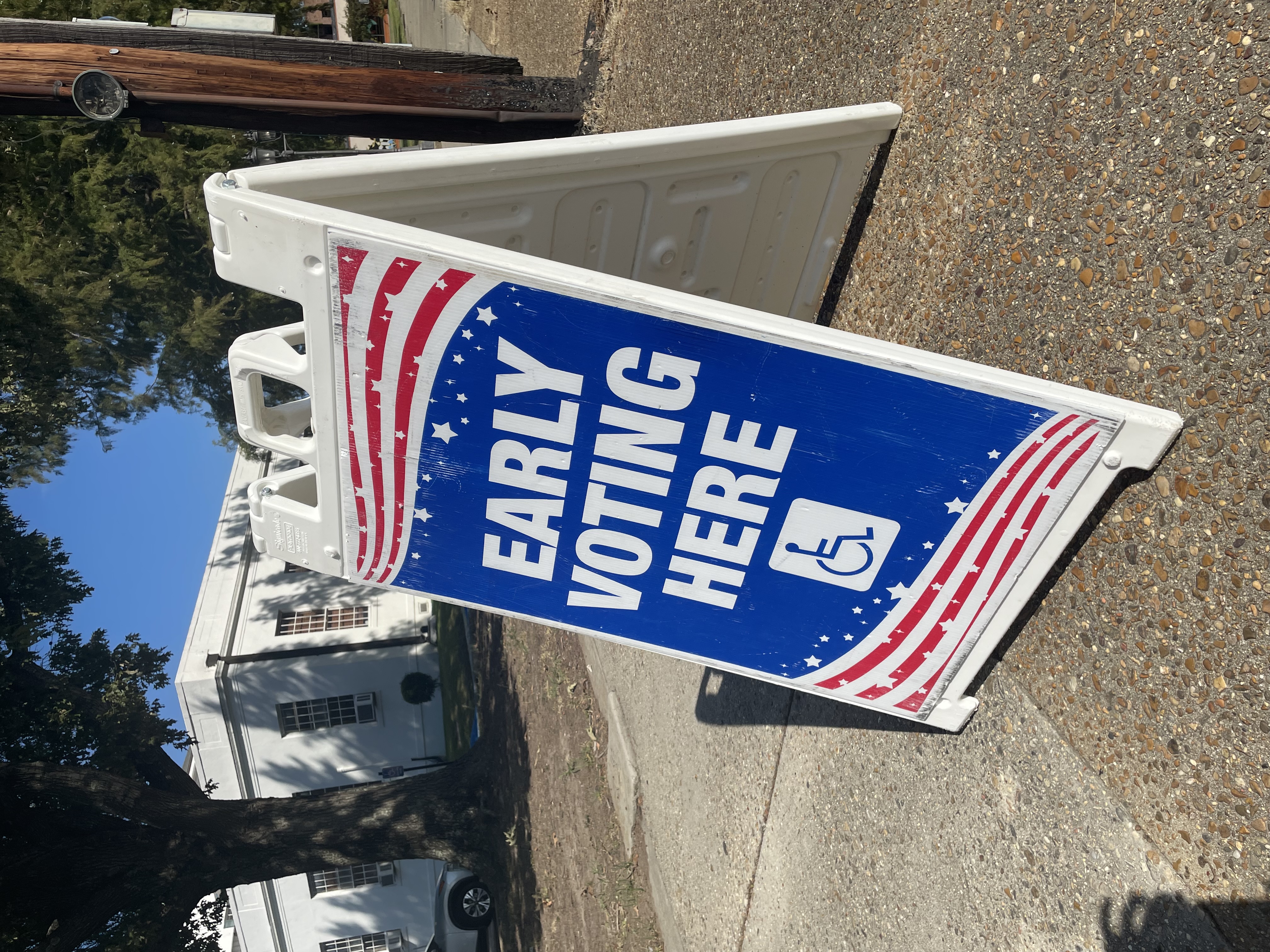 A-frame sign reading 'Early Voting Here' on a sidewalk outside a building.