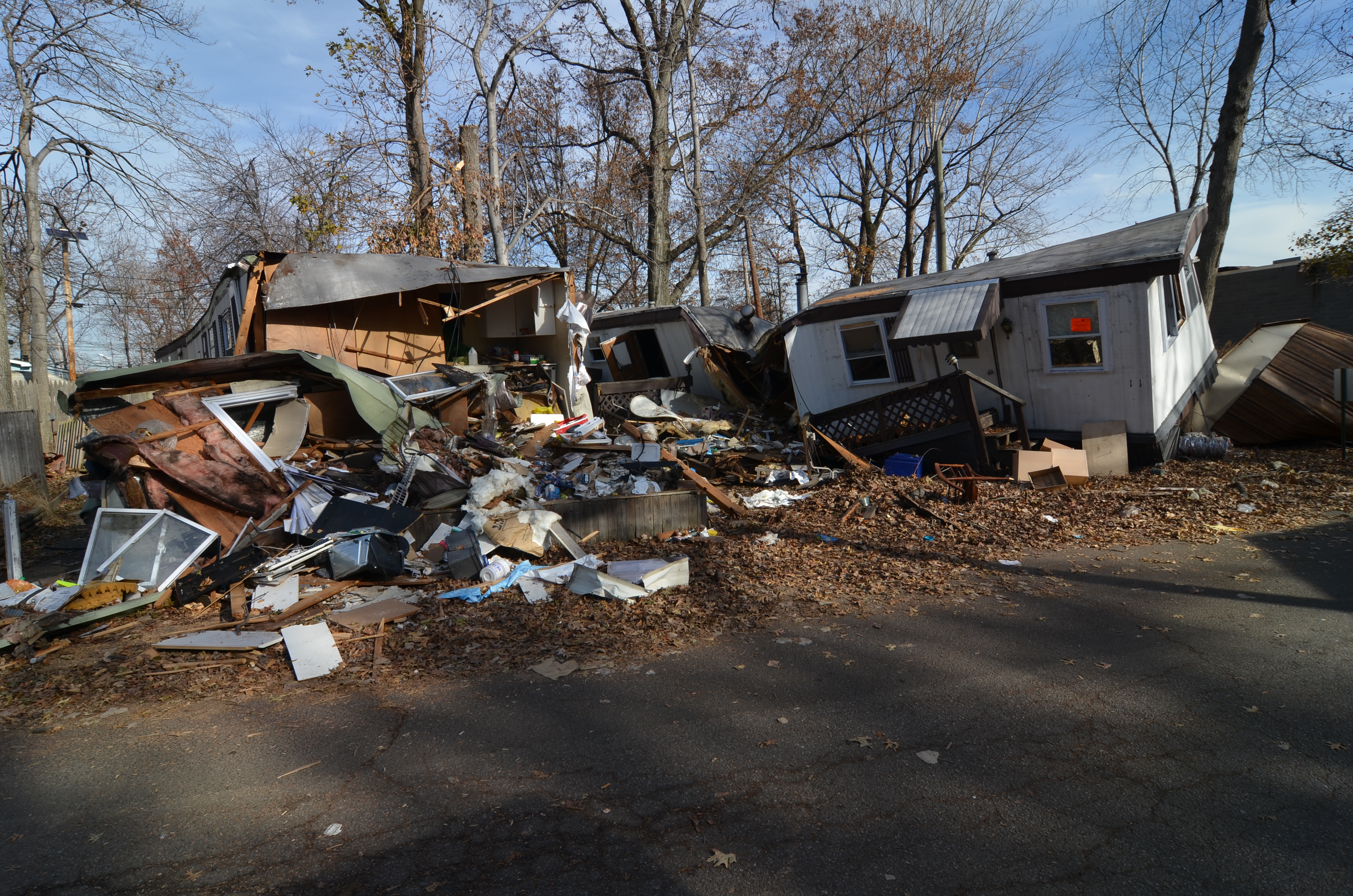 Heavily damaged homes with large debris piles along a road after a storm.