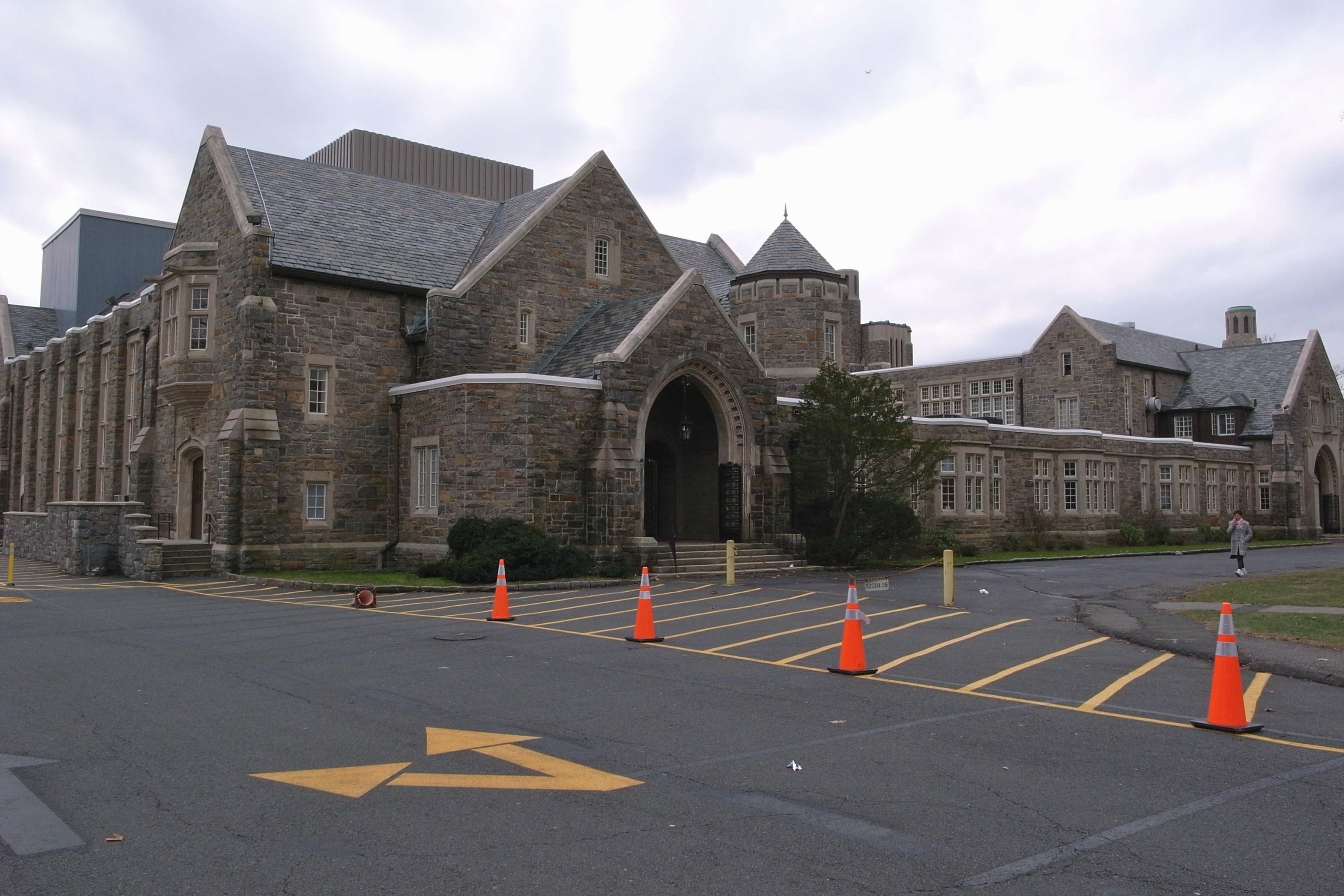 Gothic Revival stone school building with orange traffic cones in the parking lot.