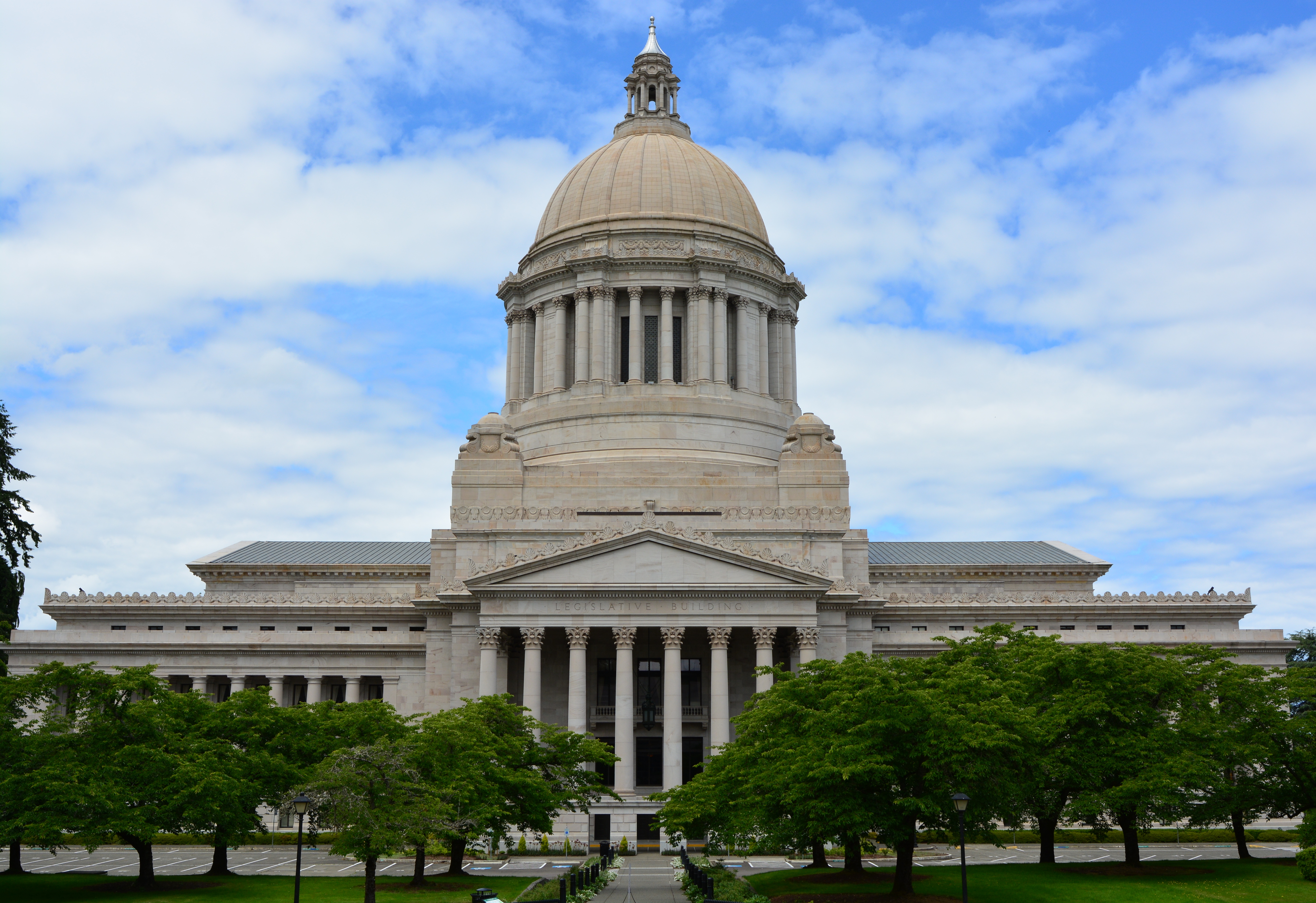 Domed state capitol building with classical columns and manicured lawn under partly cloudy sky.