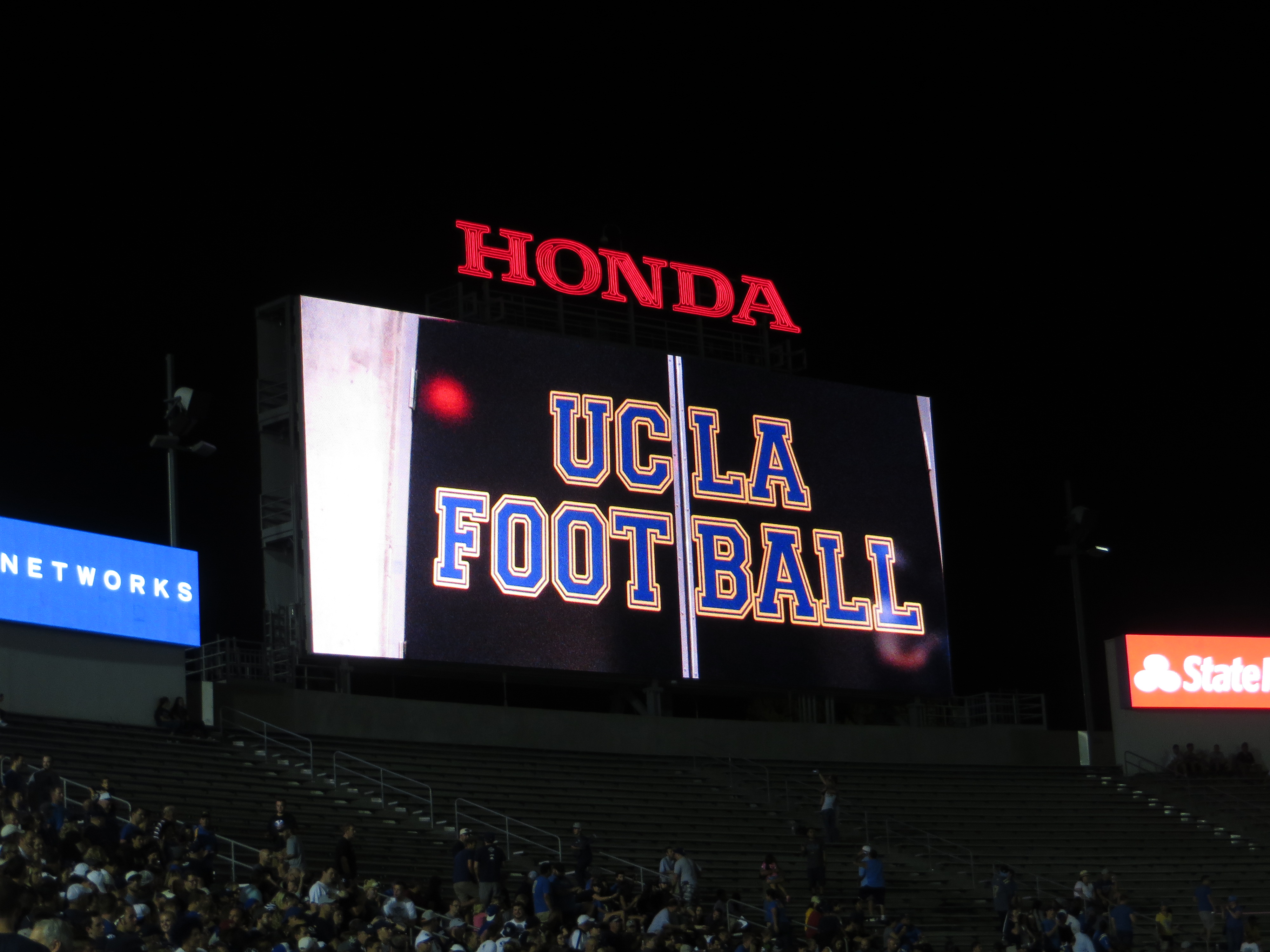 Illuminated stadium scoreboard reading 'UCLA Football' in blue and gold at night.