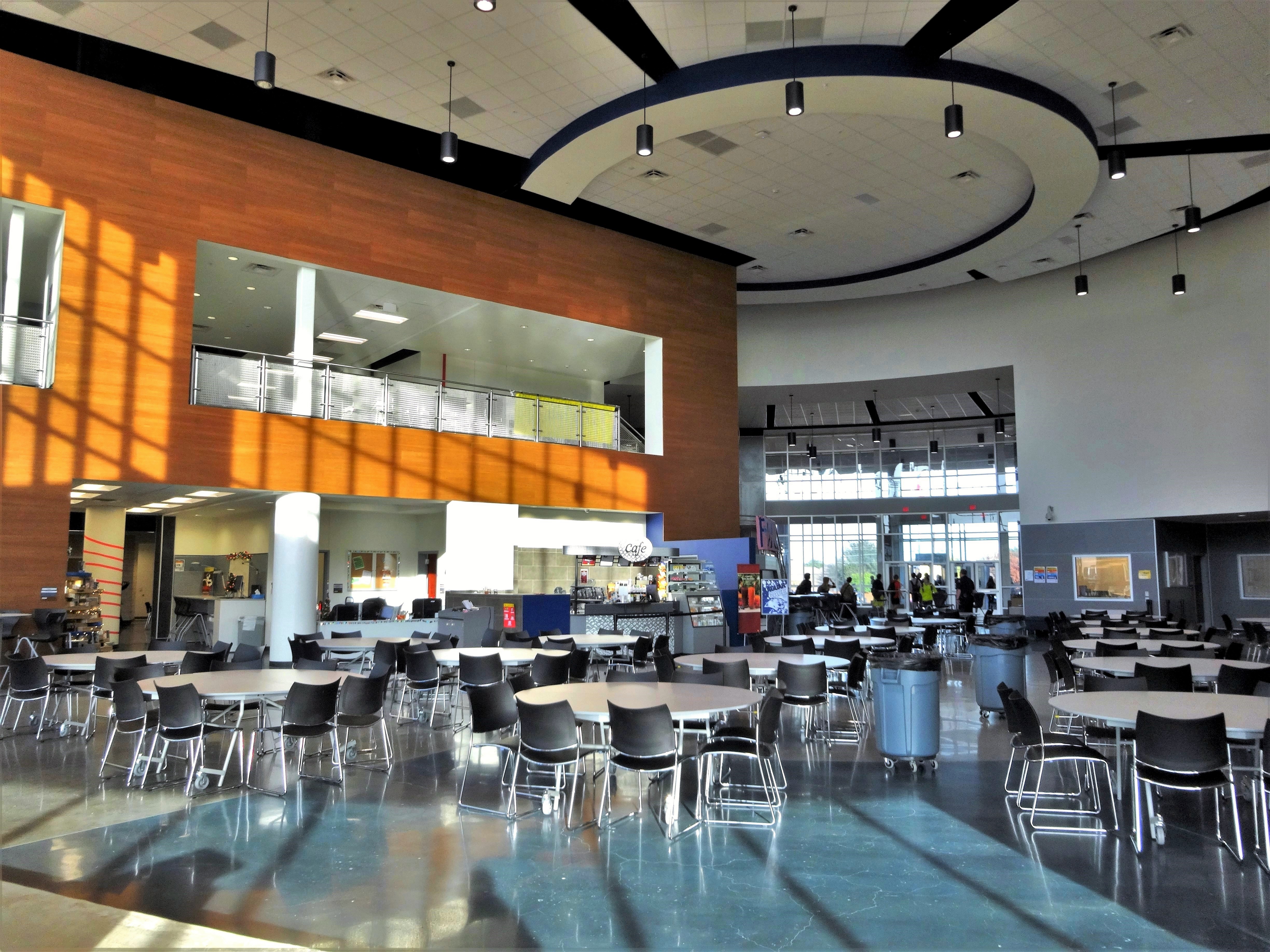 Open-plan school learning hub with round tables, pendant lighting, and large windows.