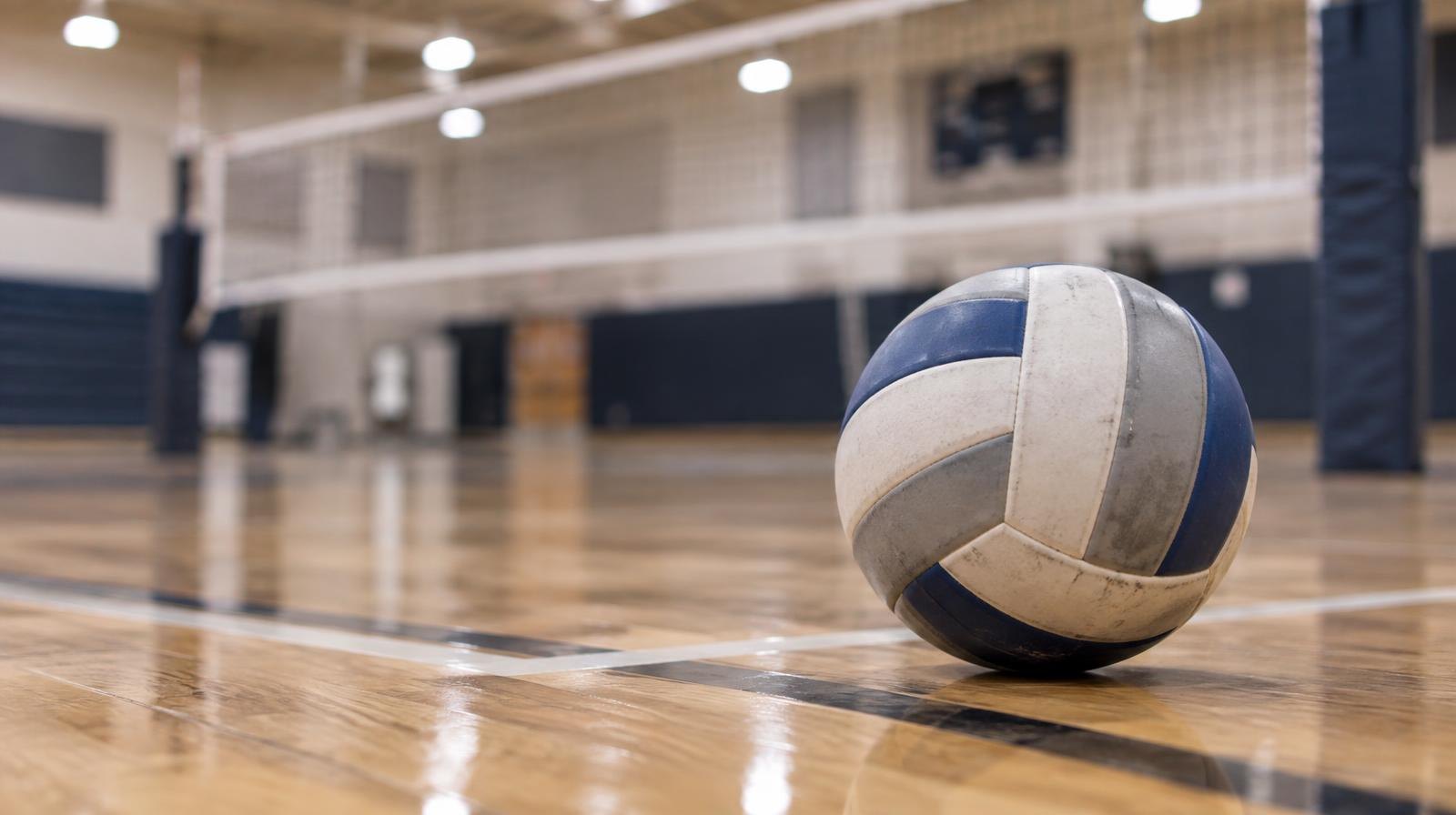 A volleyball resting on a hardwood gymnasium floor near the net.