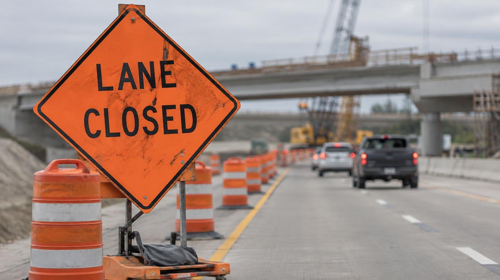 Orange traffic cones and lane closure signs narrow a highway bridge under construction.