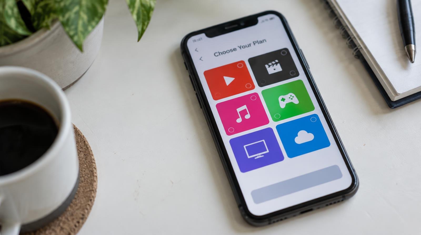 Smartphone on a white surface displaying colorful app icon tiles on its screen.