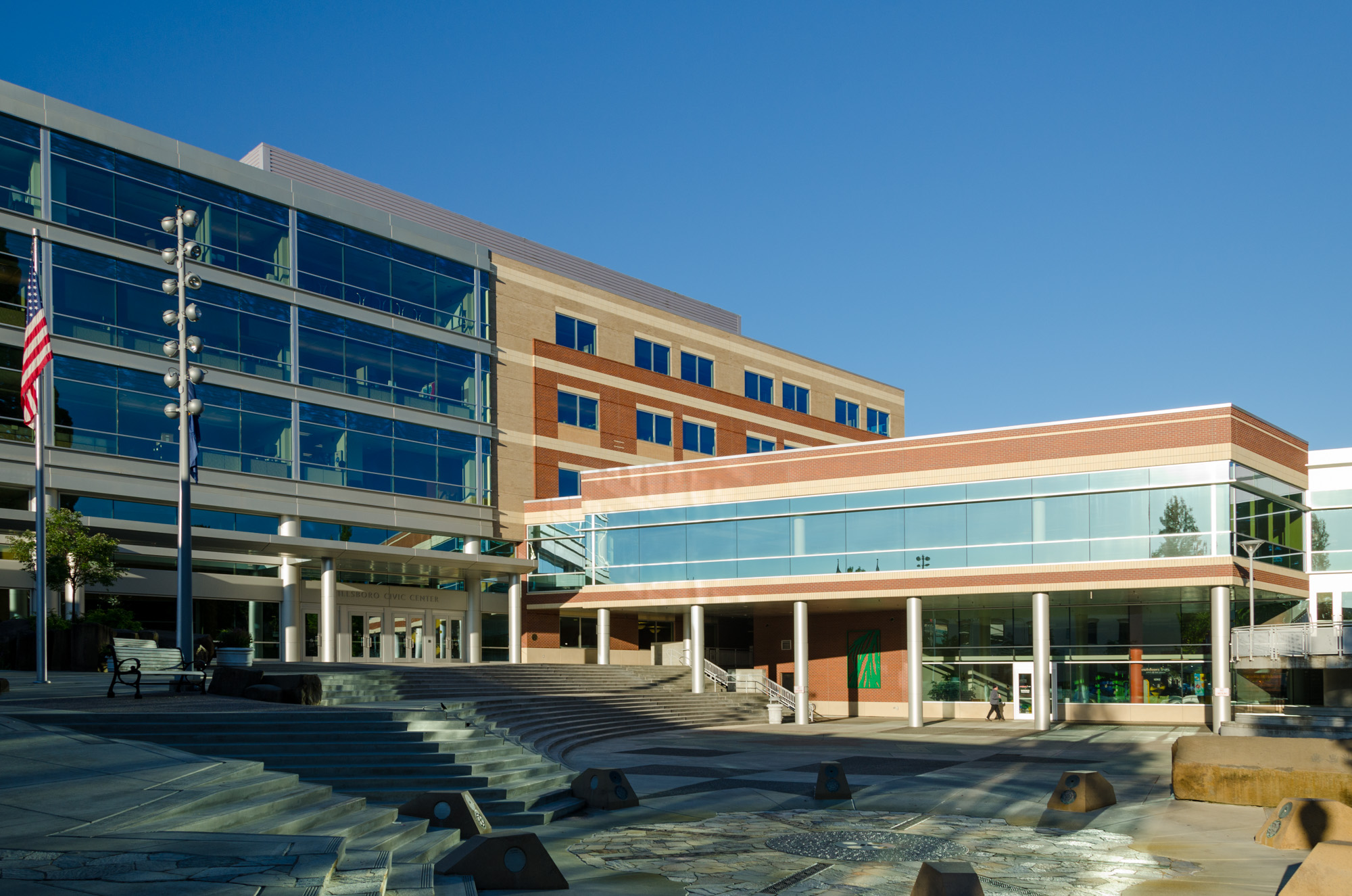 Modern multi-story civic building with glass facade, brick accents, and an American flag out front.