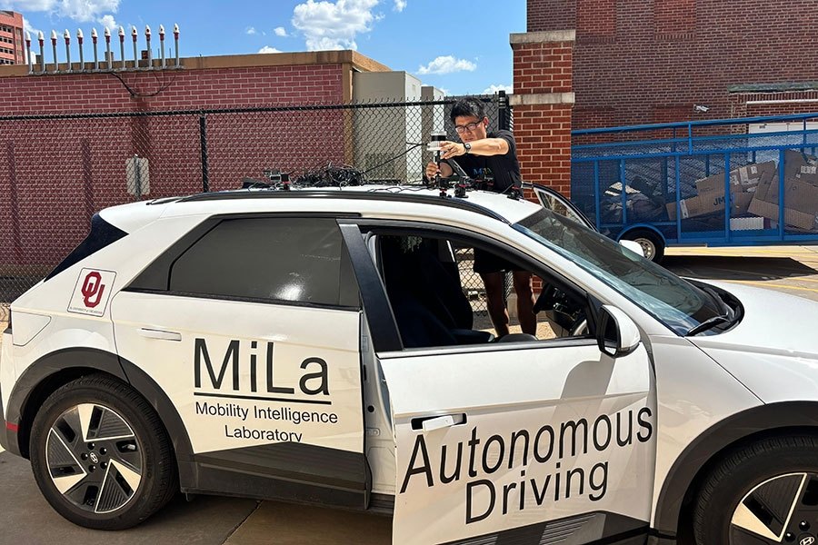 Person installing roof equipment on a white sedan labeled Autonomous Driving.