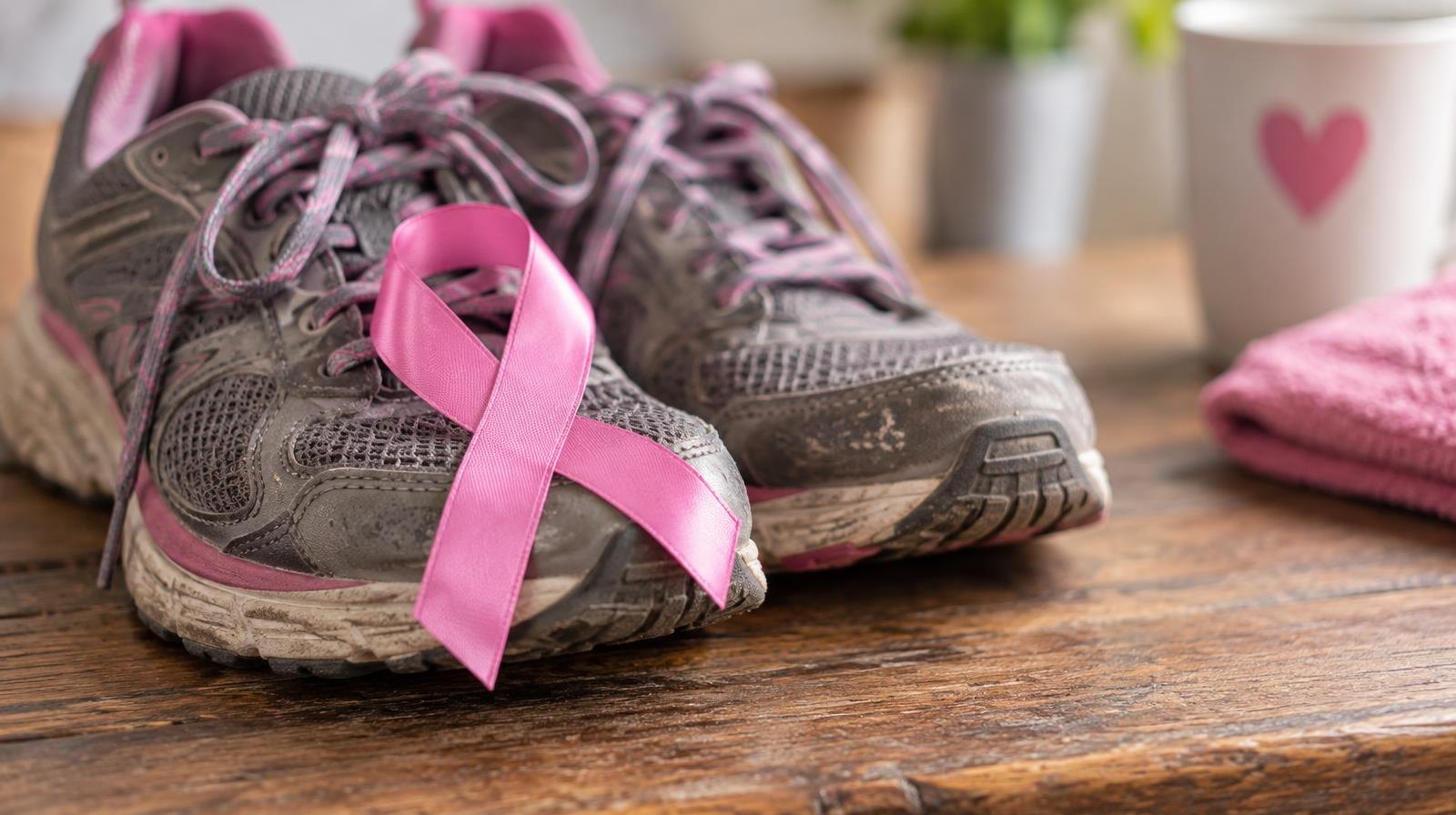 Pink breast cancer awareness ribbon resting on a pair of worn walking shoes.