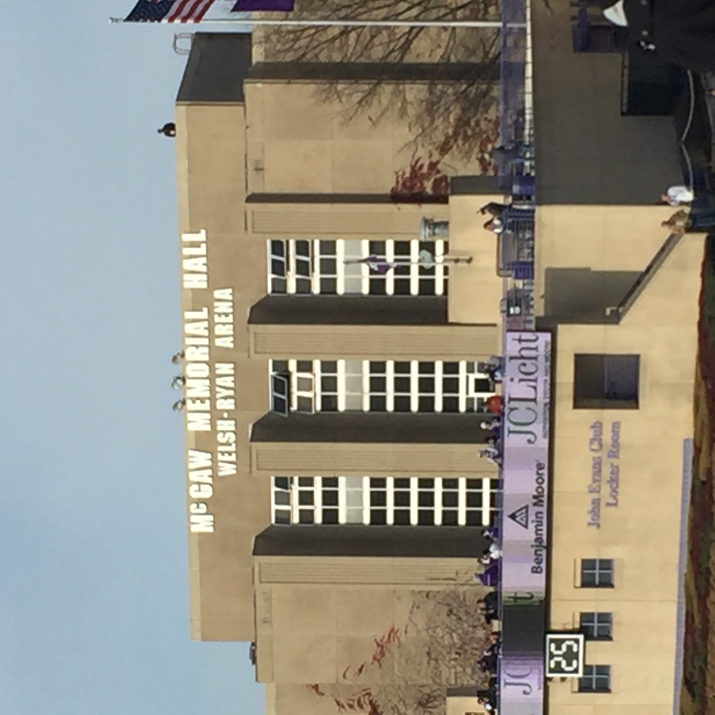 Exterior of a large arena building with signage, an American flag, and sponsor banners on a clear day.