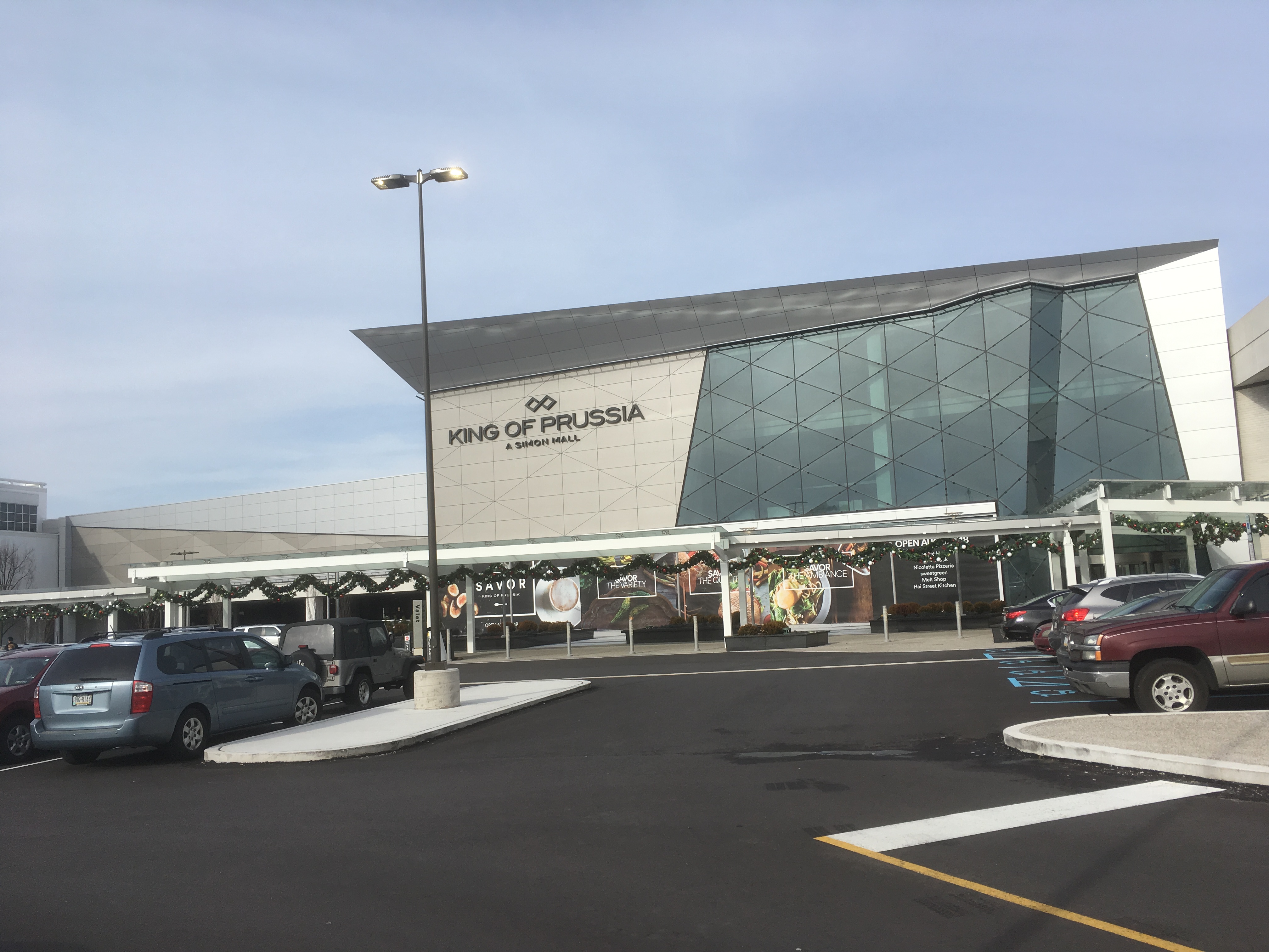 Exterior entrance of a large shopping mall with a glass and steel facade.