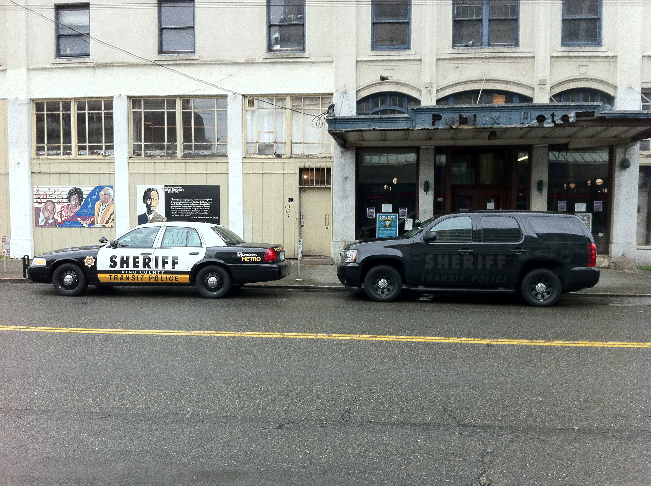 A white Sheriff Transit Police sedan and a dark Sheriff SUV parked on a city street.