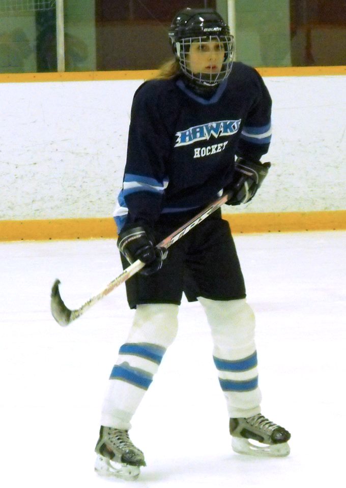 Female ice hockey player in a dark blue jersey skating on an indoor rink.