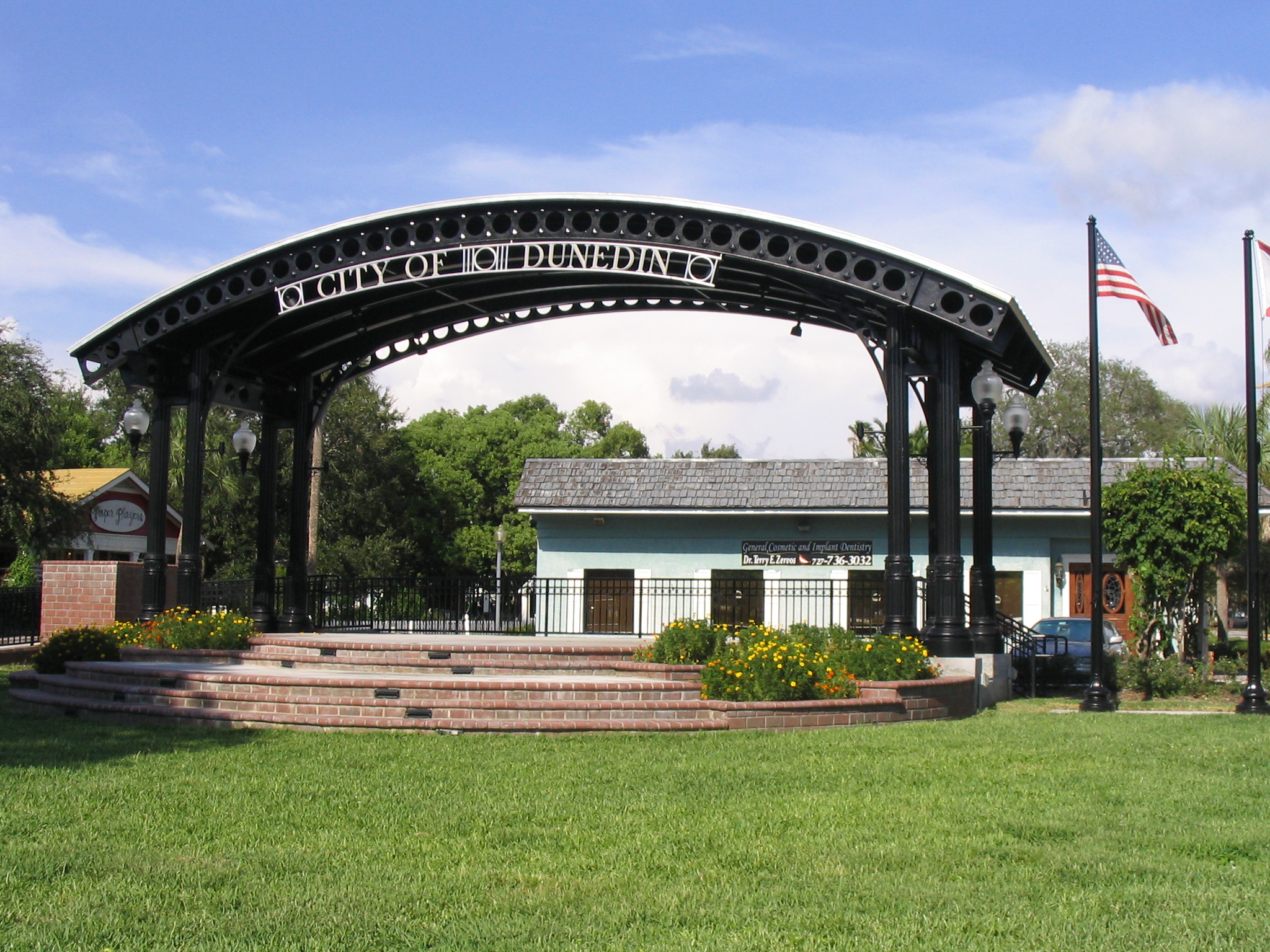 Decorative metal arch reading City of Dunedin over a brick bandshell stage in a park.