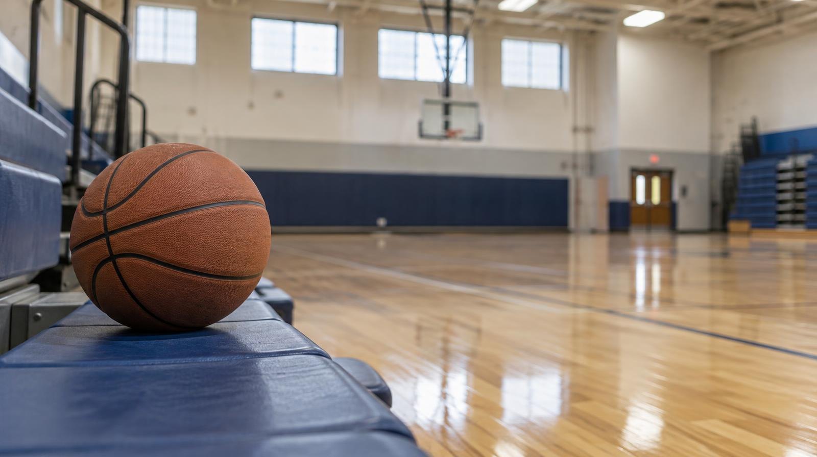 Empty school gymnasium with hardwood floors, basketball hoops, and folded bleachers.