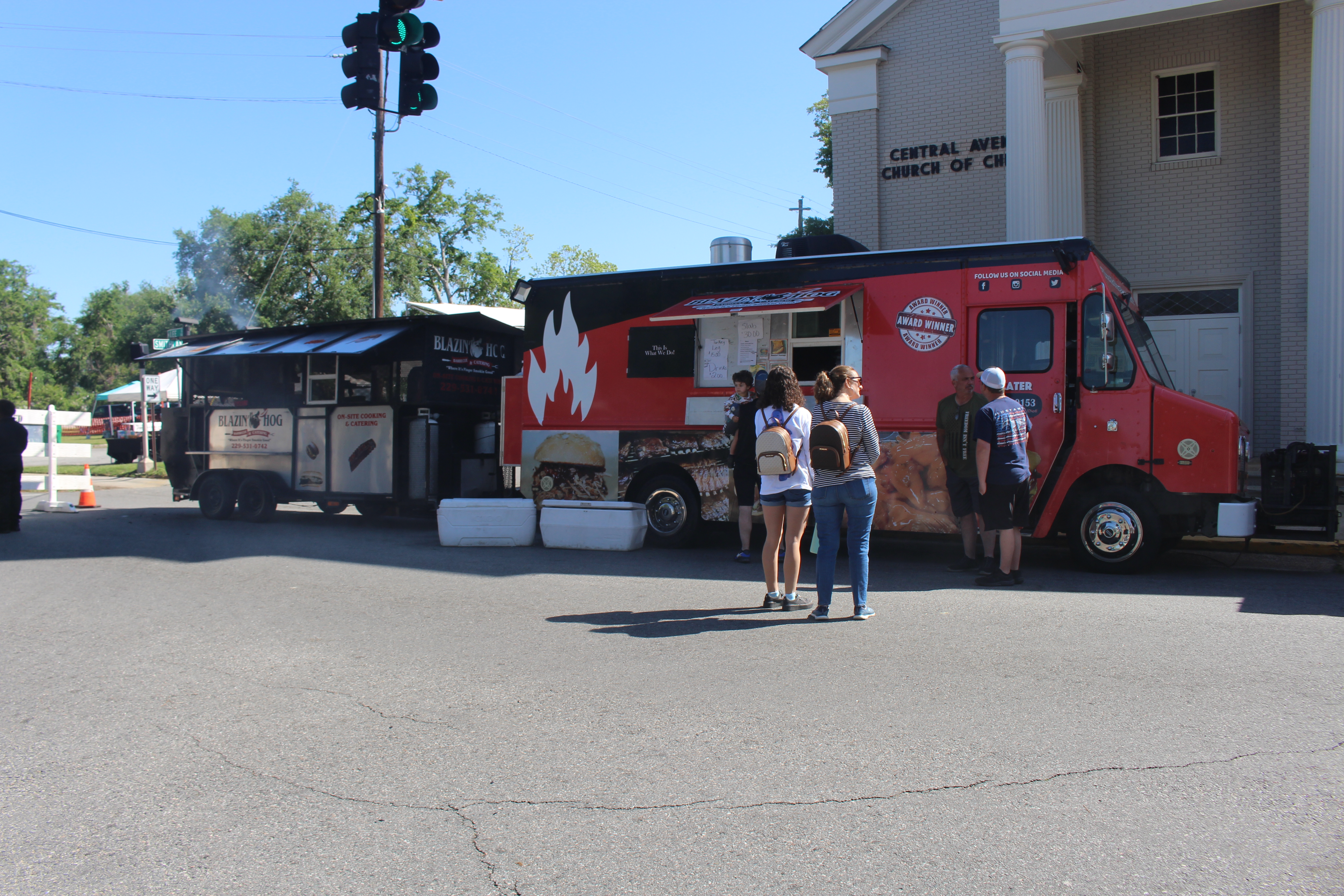 Two food trucks parked side by side with customers standing in line to order.