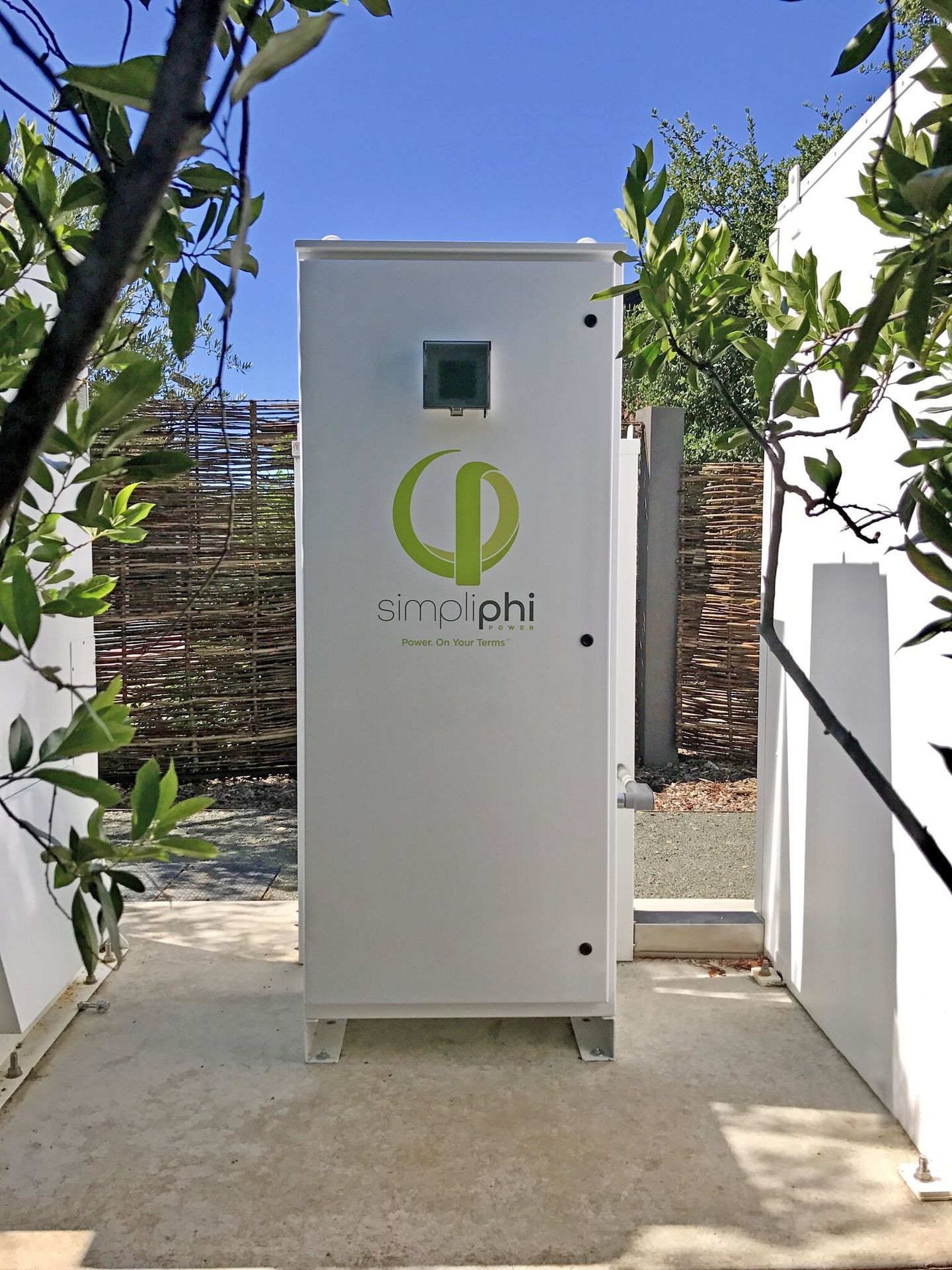 White outdoor battery storage cabinet mounted on a concrete pad beside a wall.