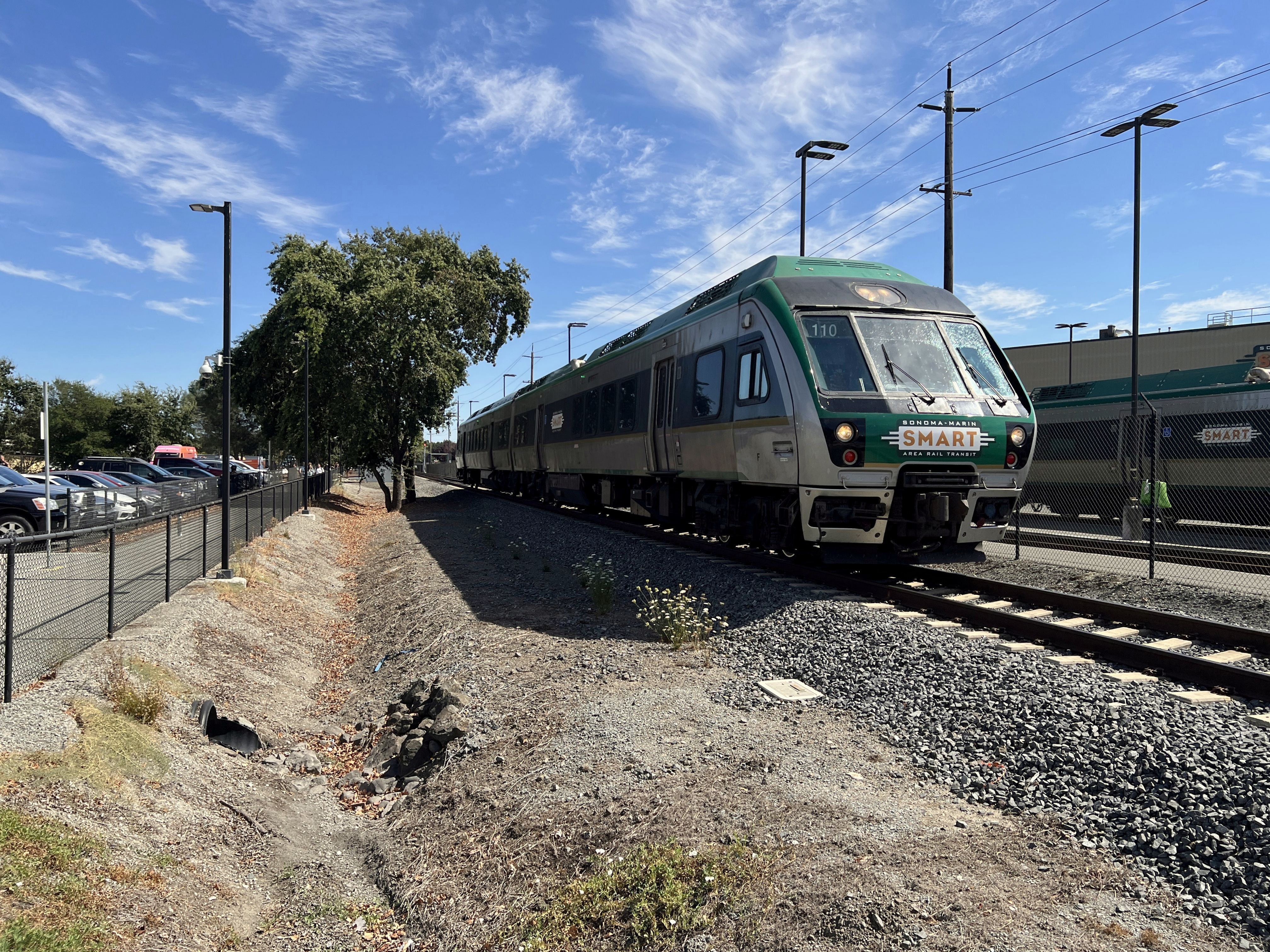 A green and silver SMART commuter train moving along tracks near a station.