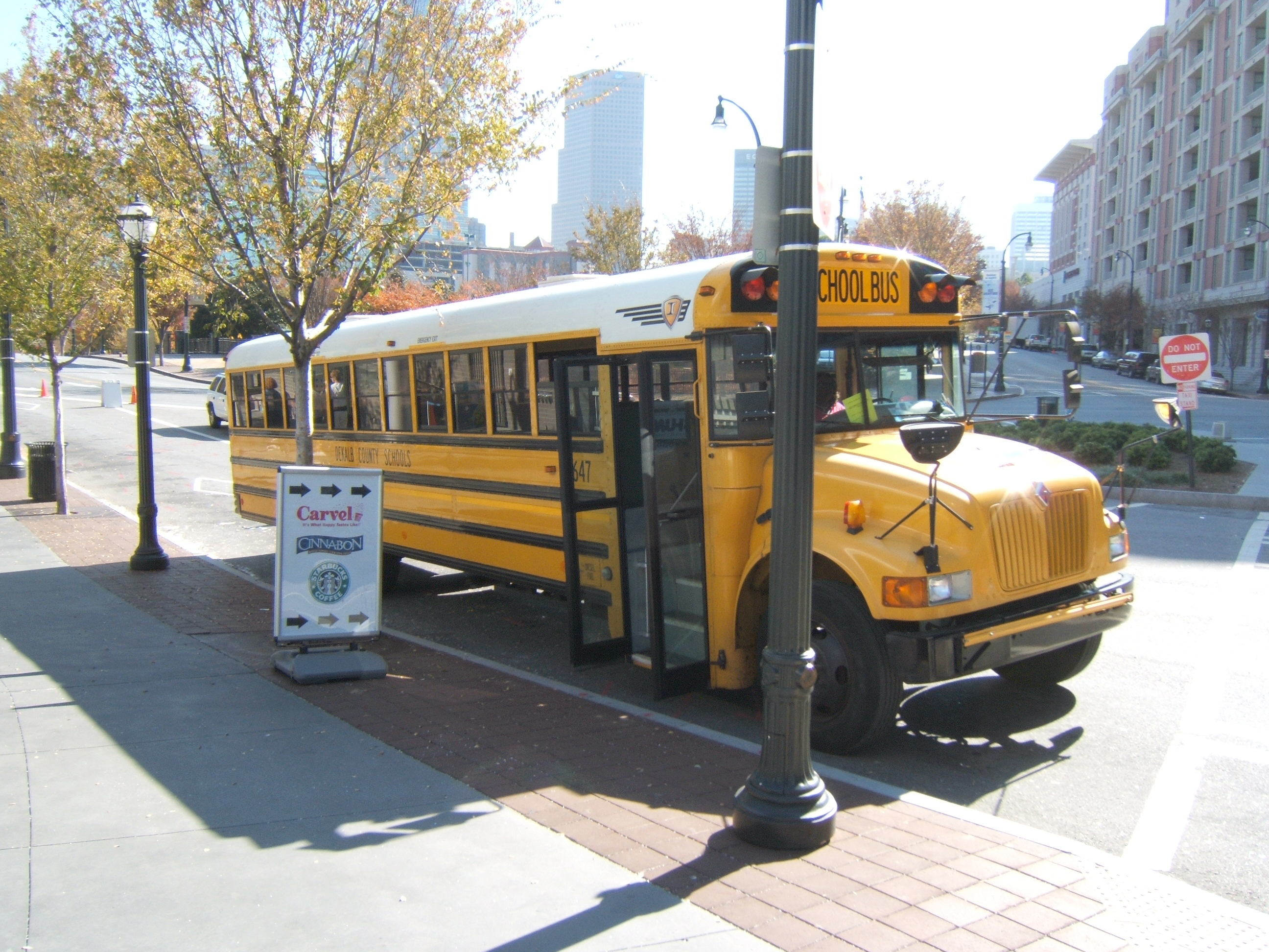 Yellow school bus parked on a city sidewalk with trees and buildings behind it.