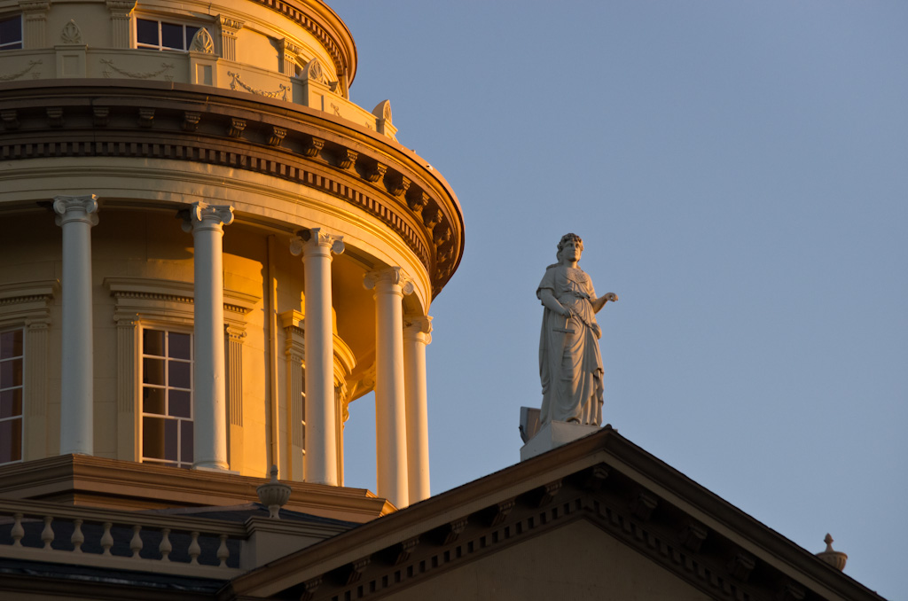 Neoclassical courthouse dome with white columns and a rooftop statue at golden hour.
