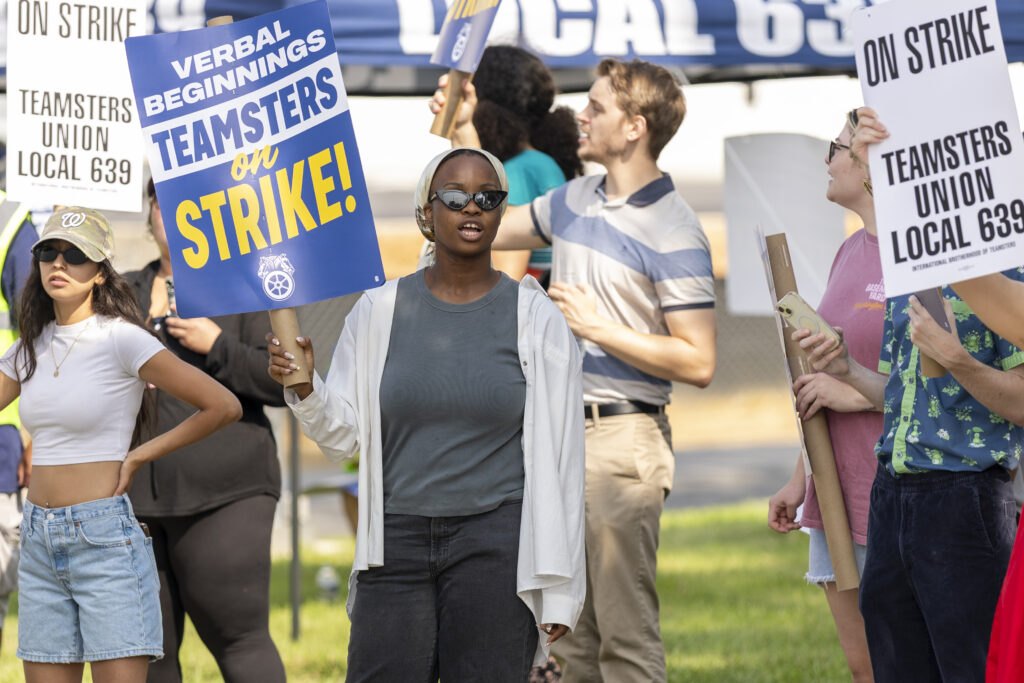 Workers holding Teamsters on Strike signs chant on an outdoor picket line.