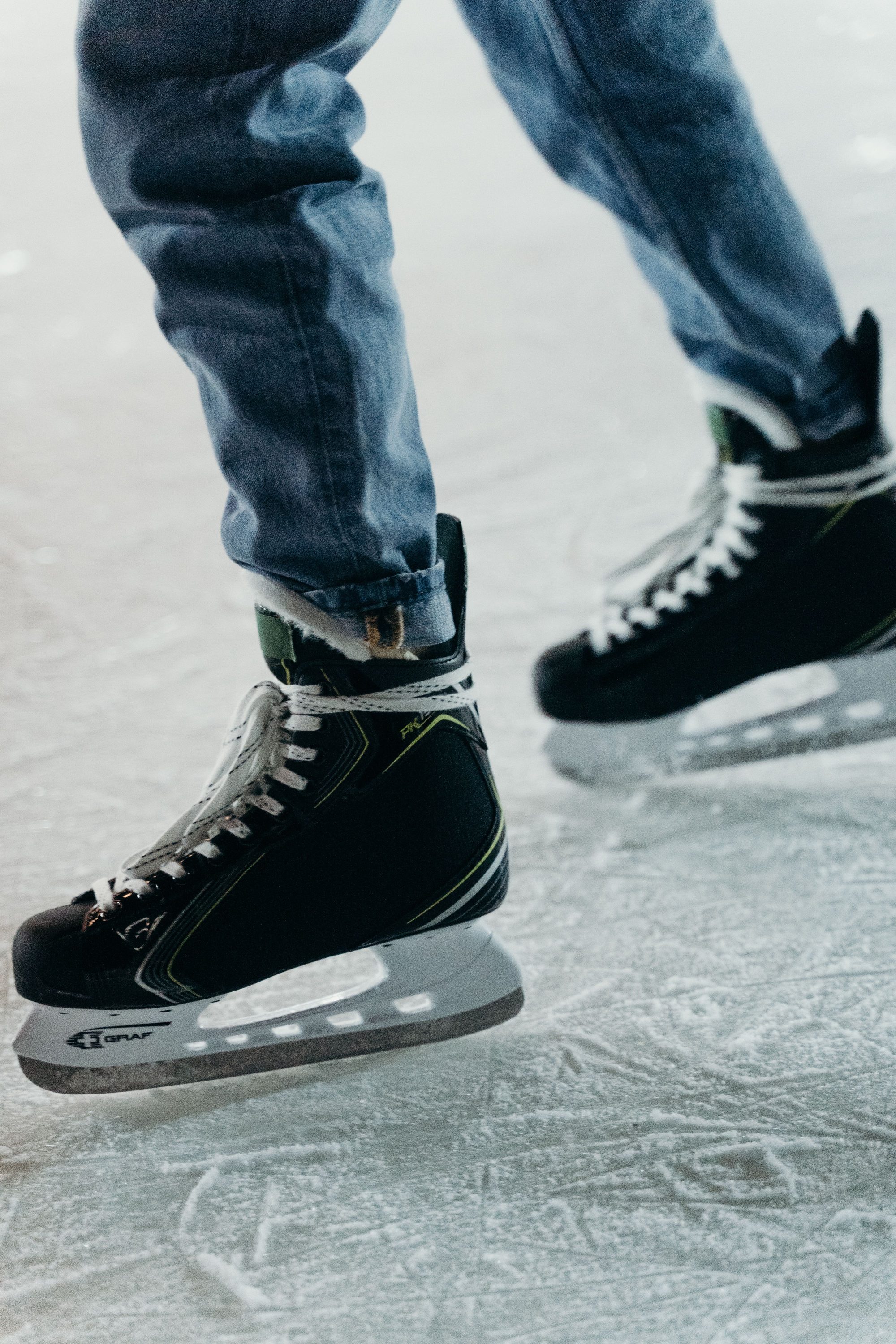 Person wearing jeans and ice skates on an ice rink, illustrating winter sports activity.