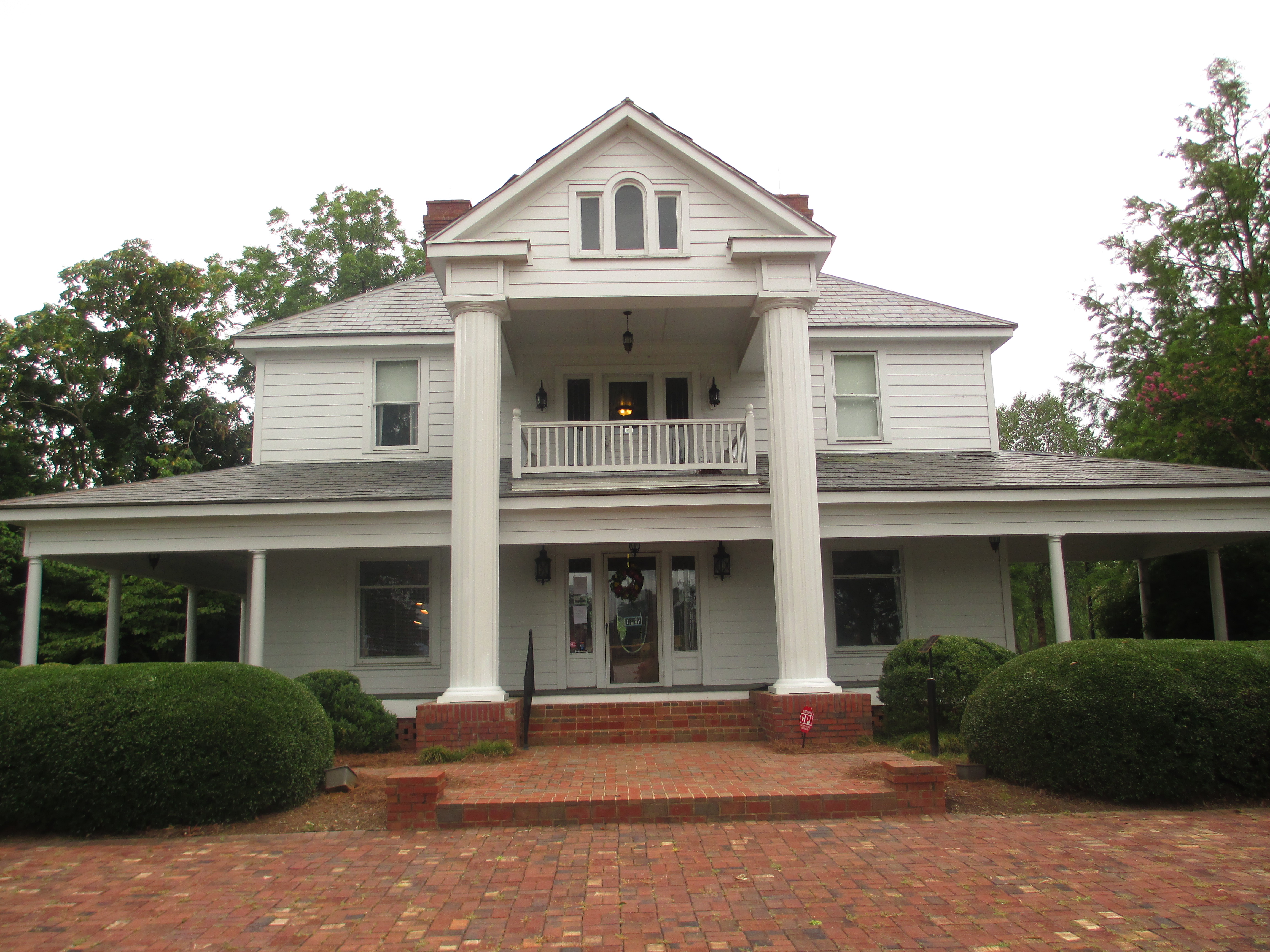 Two-story white colonial building with large columns and manicured shrubs out front.