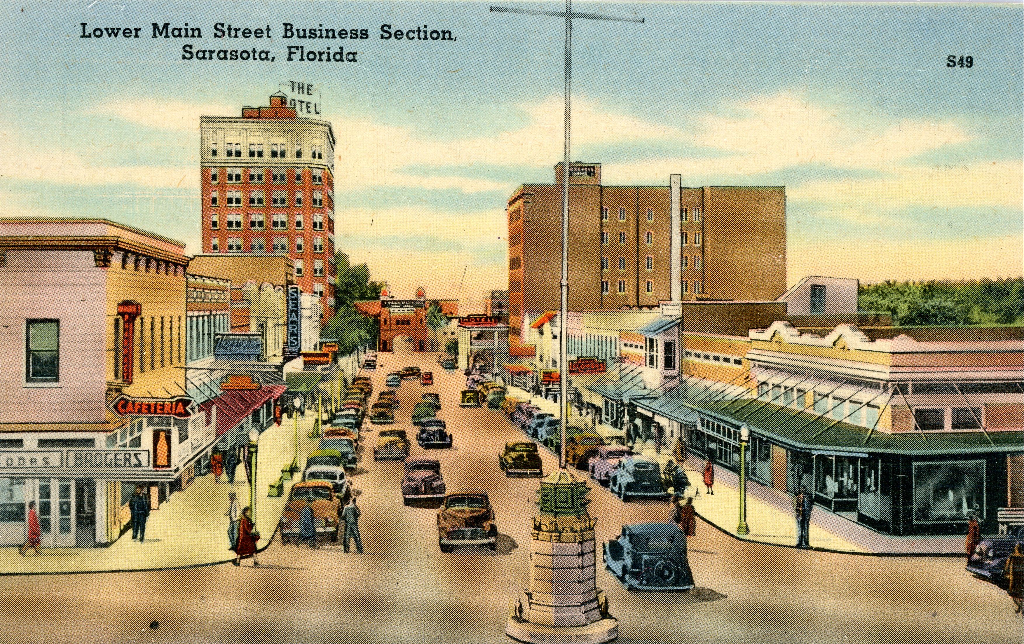 Colorized vintage postcard showing a wide commercial street lined with storefronts and parked cars.