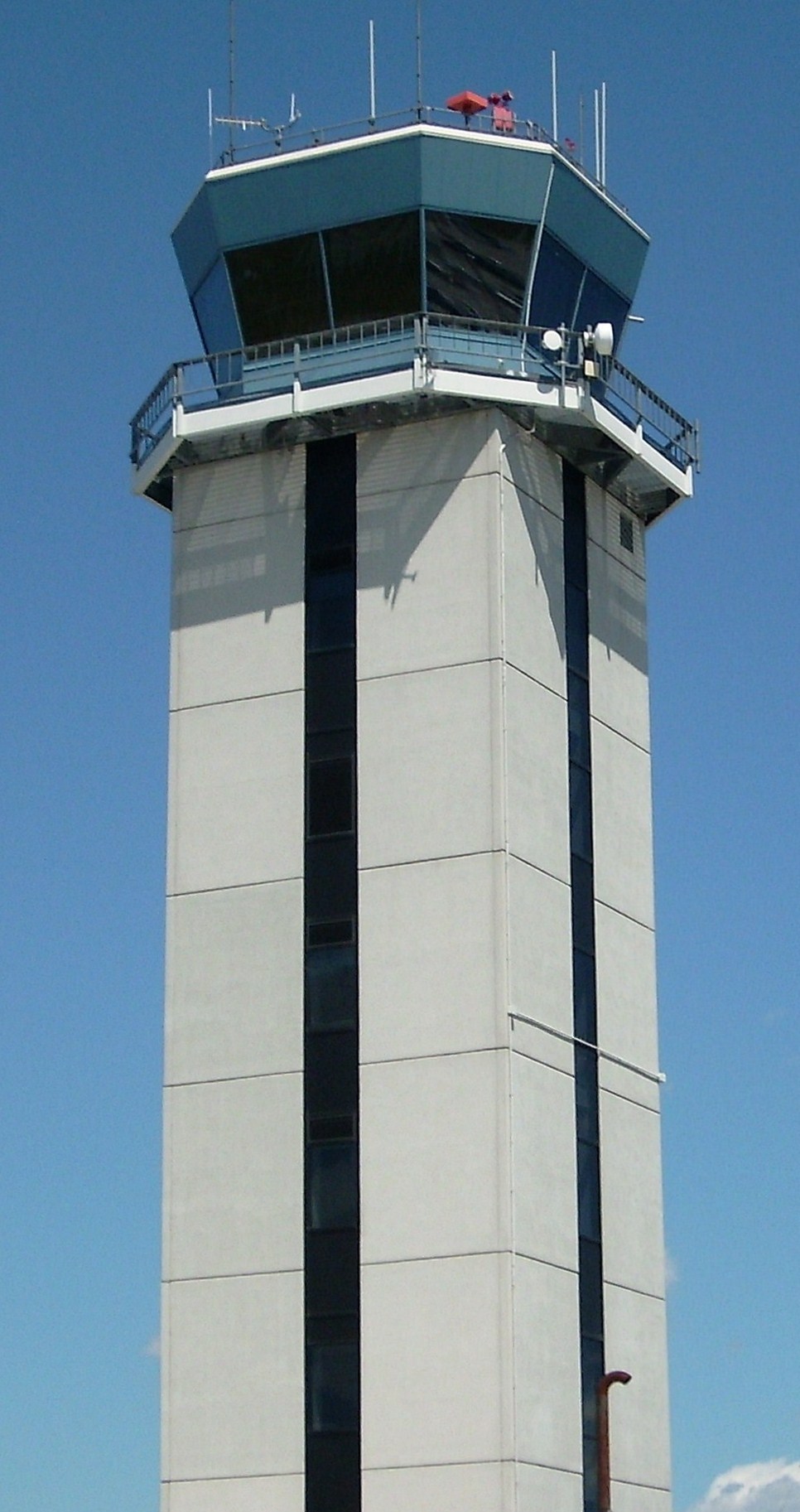 Tall concrete air traffic control tower with glass-enclosed cab against a clear blue sky.