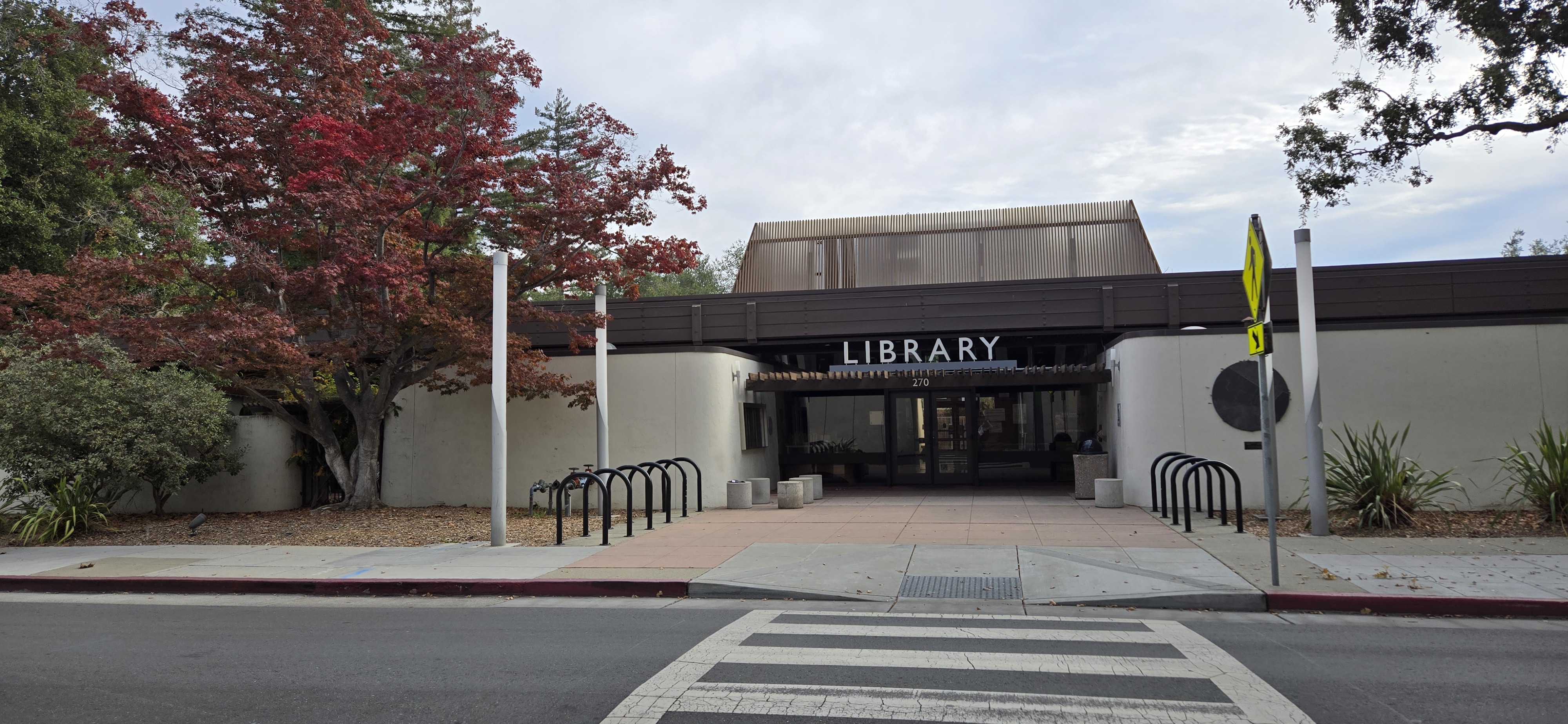 Exterior entrance of a public library building with a sign reading 'Library' and bicycle racks out front.