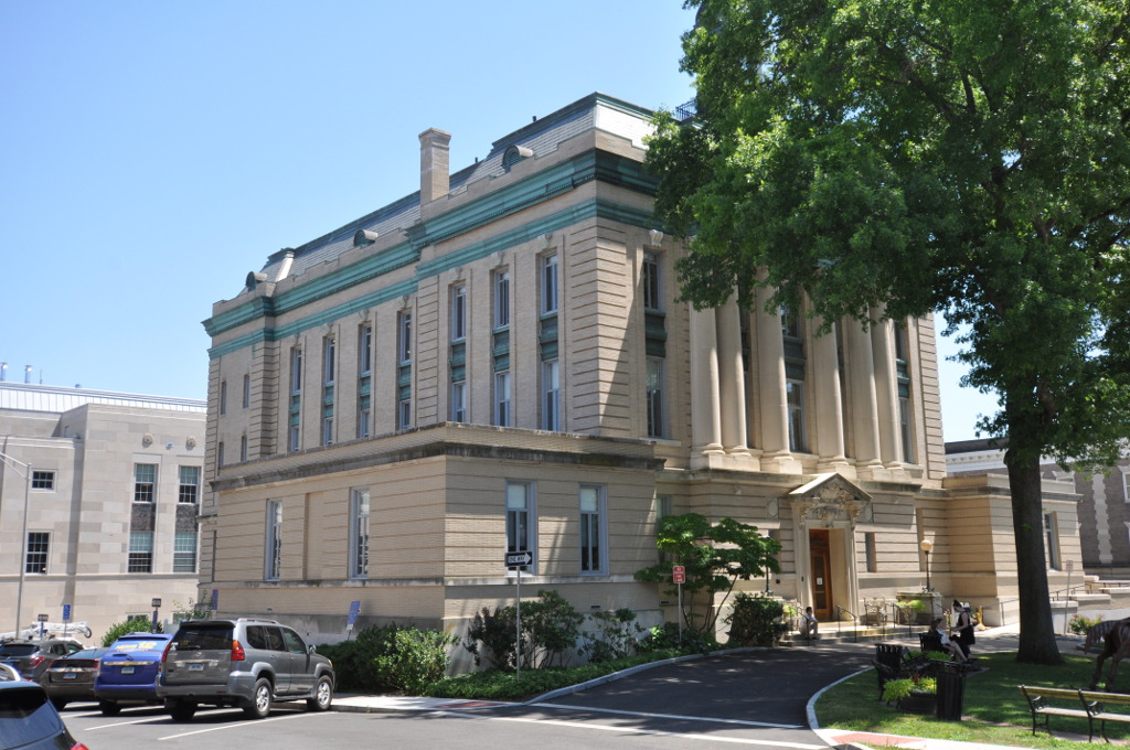 Neoclassical government building with large columns and tan stone facade under a clear sky.