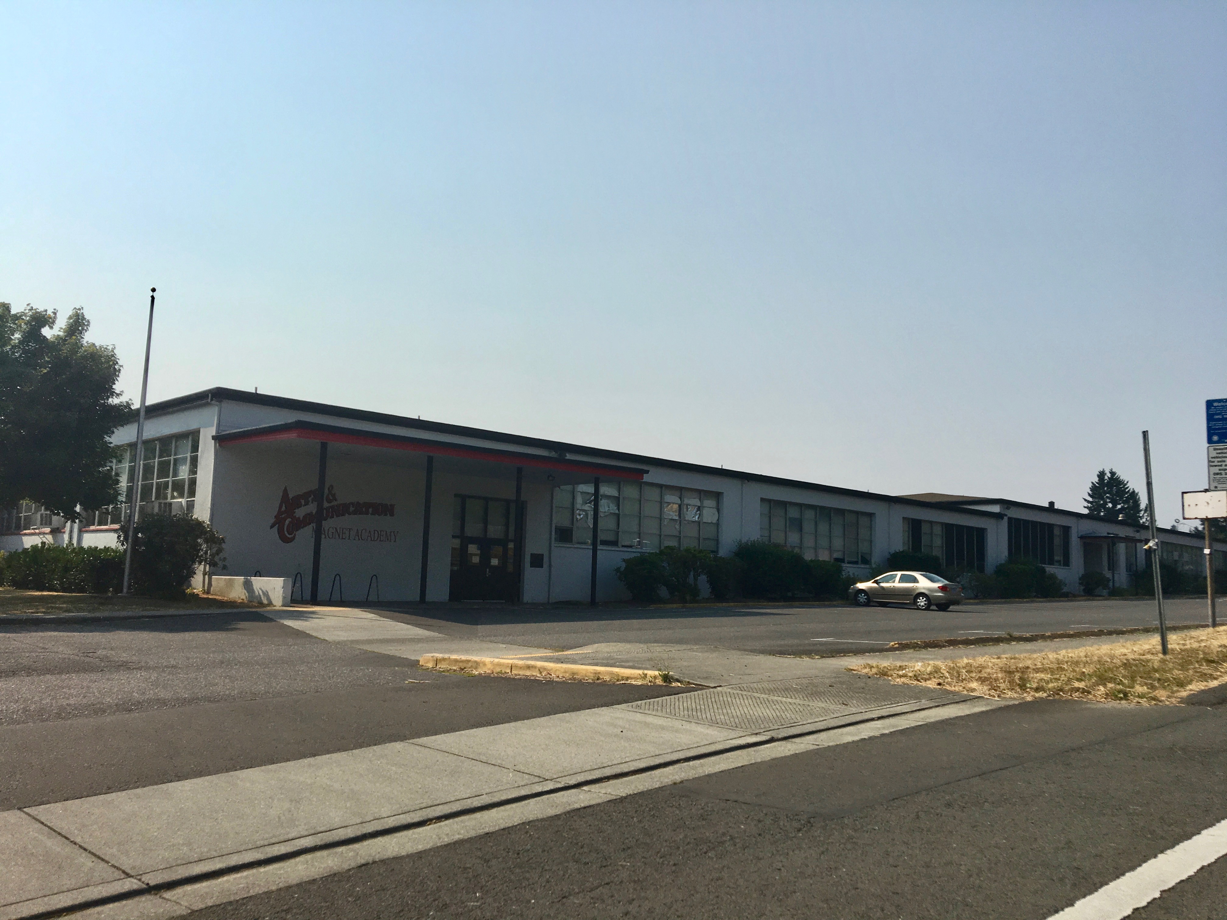 Single-story school building with red roofline trim and a school name sign in front.