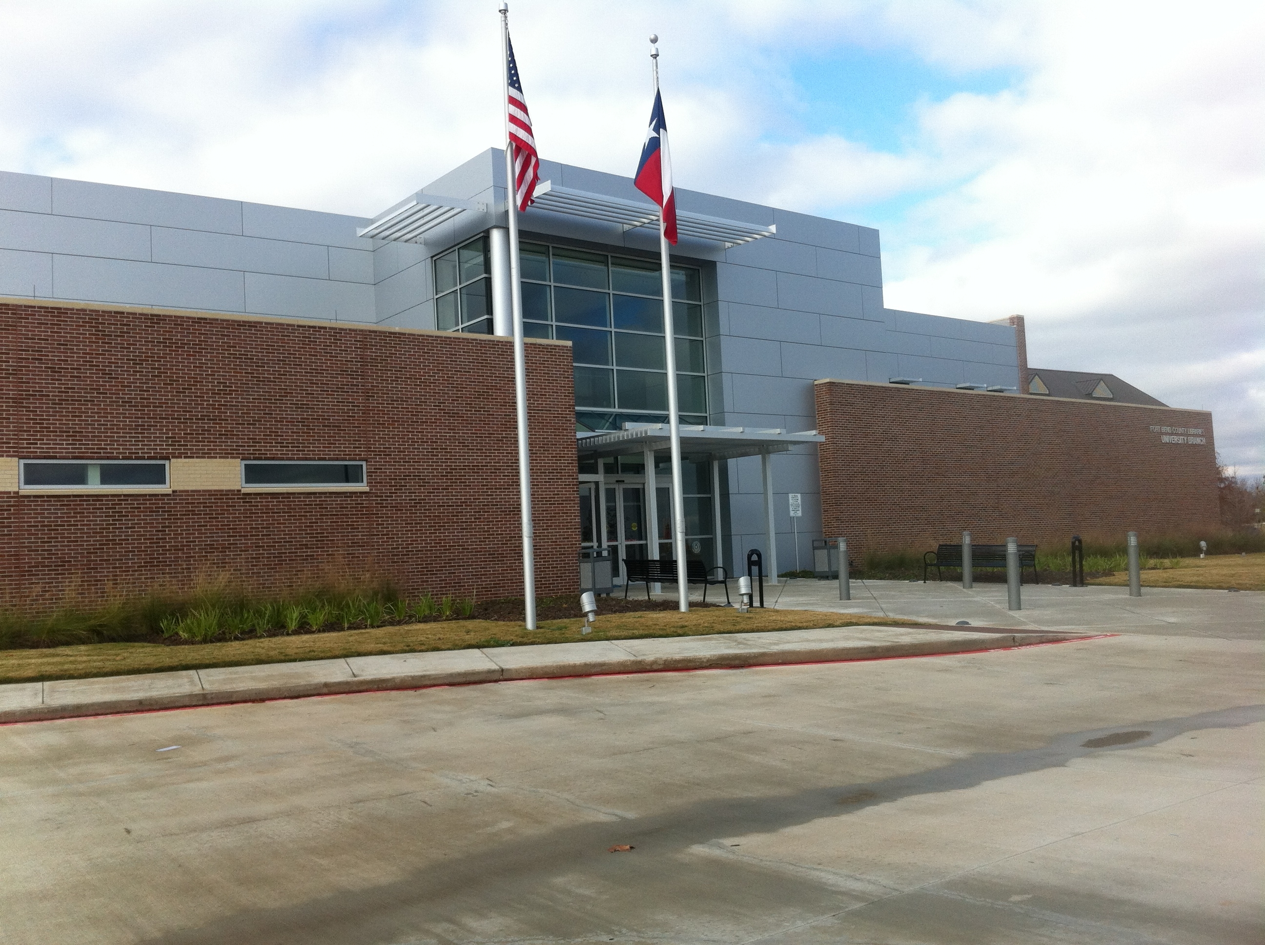 Modern brick library building with American and Texas flags on a flagpole outside.