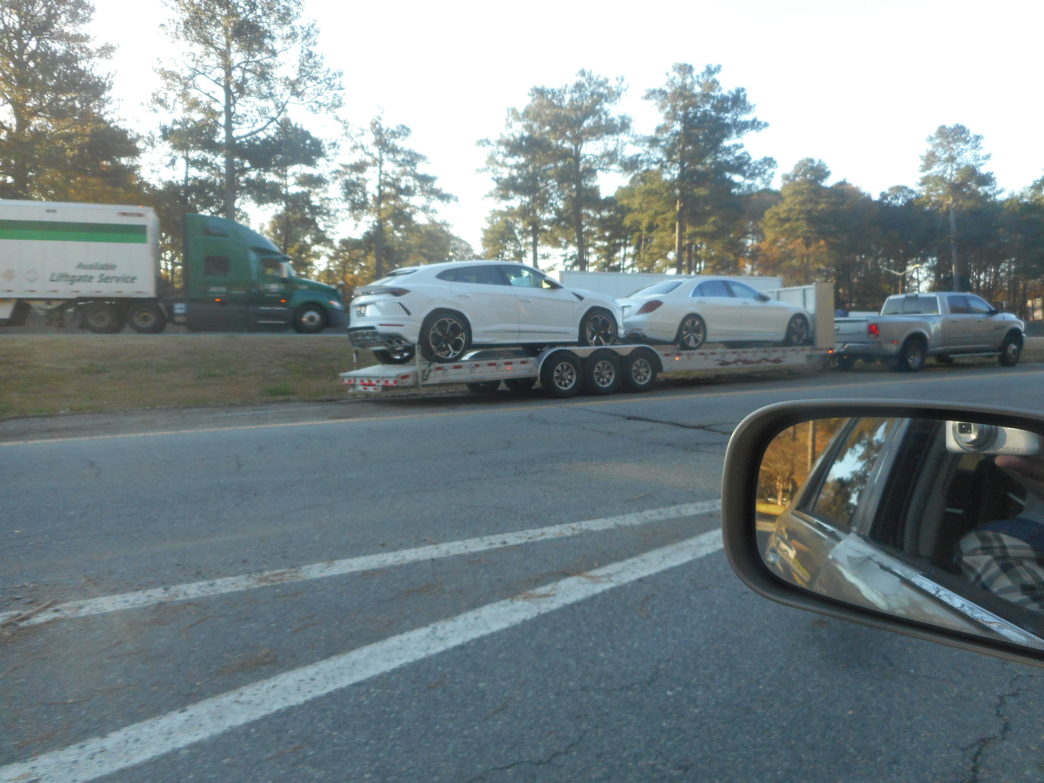 A pickup truck tows a flatbed trailer carrying two cars at a rest area.