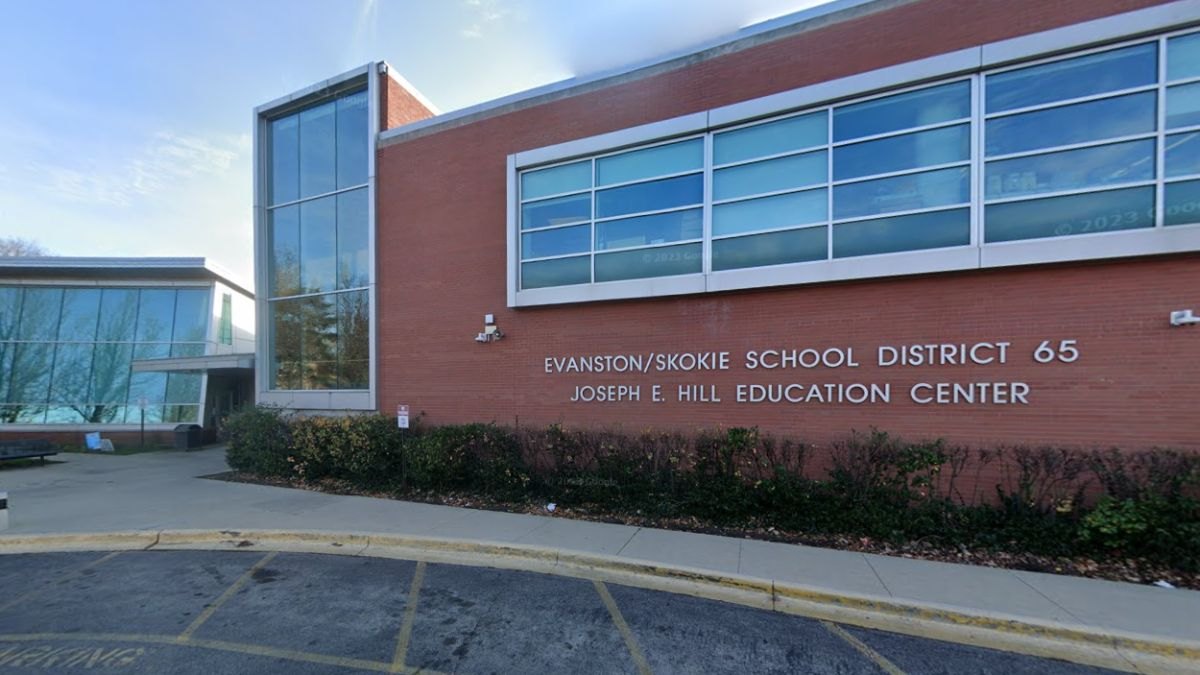 Red brick school district administration building with large windows and a parking lot in front.