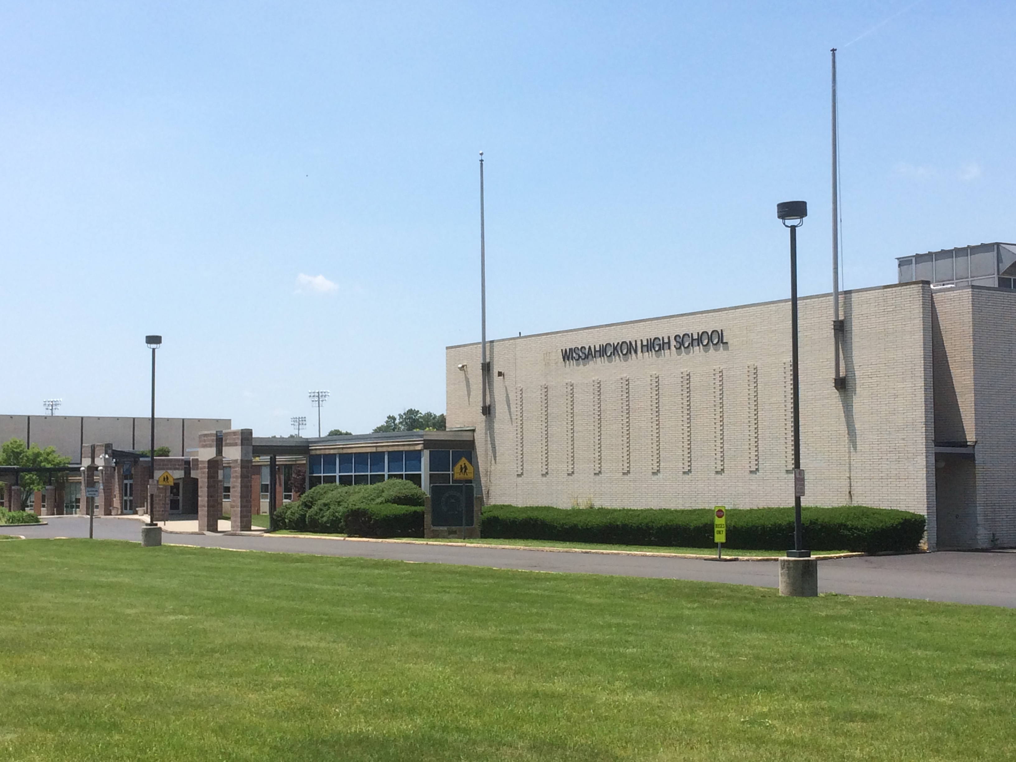 Front exterior of a brick high school building with flagpoles and a green lawn.