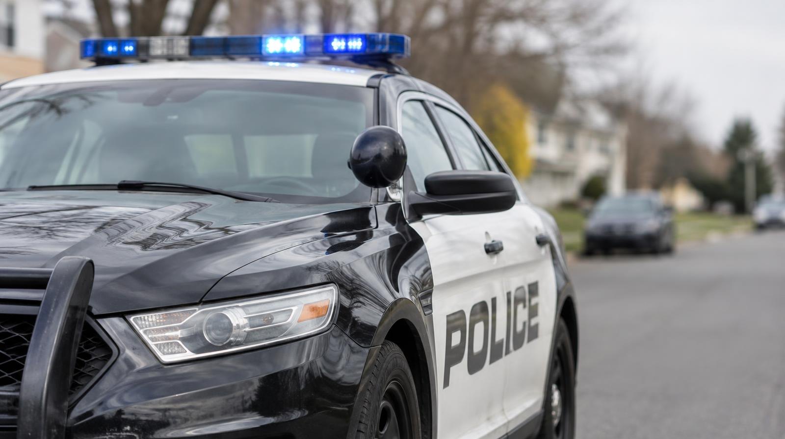 Marked police patrol car with a blue light bar parked on a quiet street.