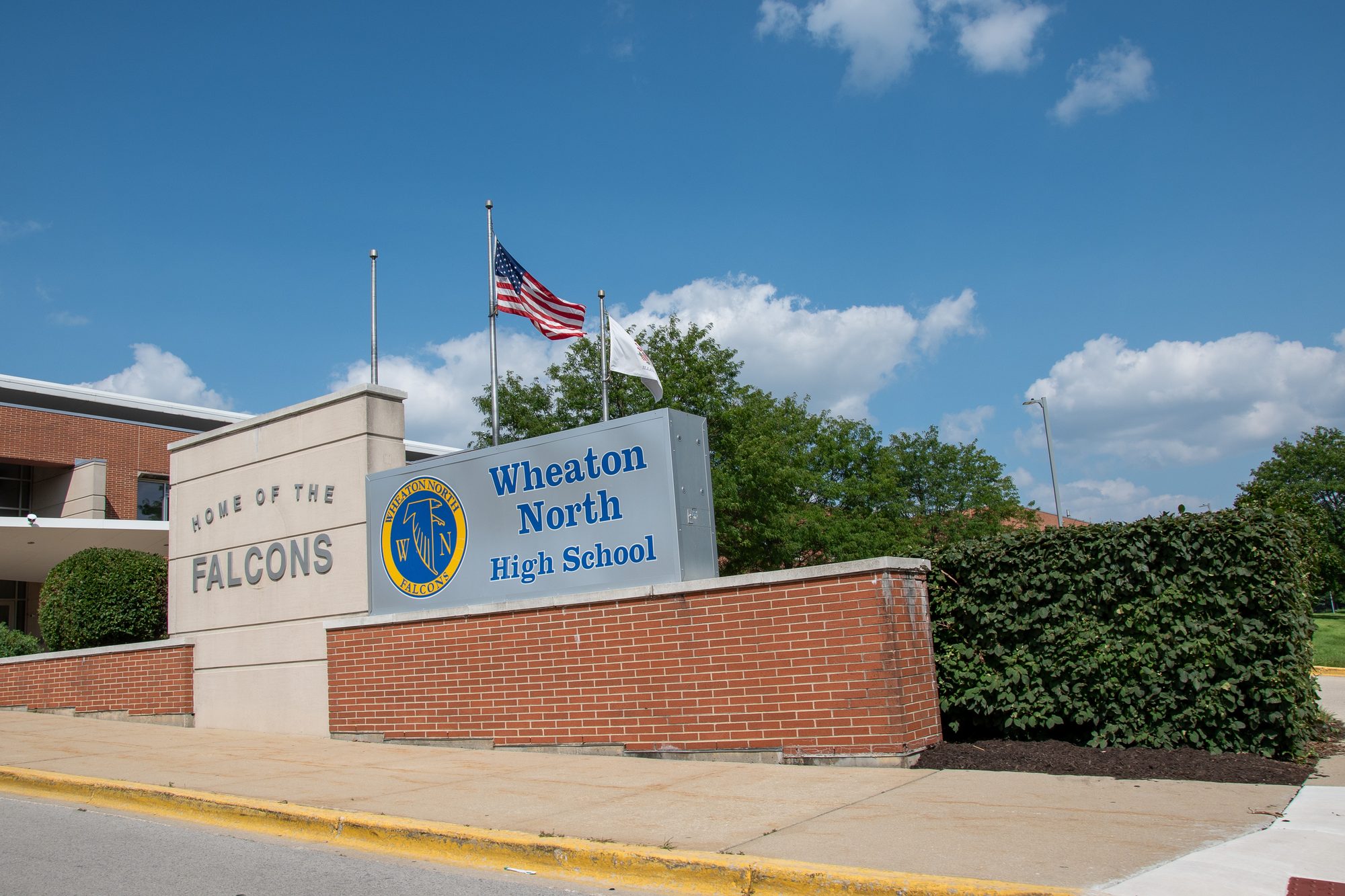 Brick sign reading Home of the Falcons outside a high school building with an American flag.