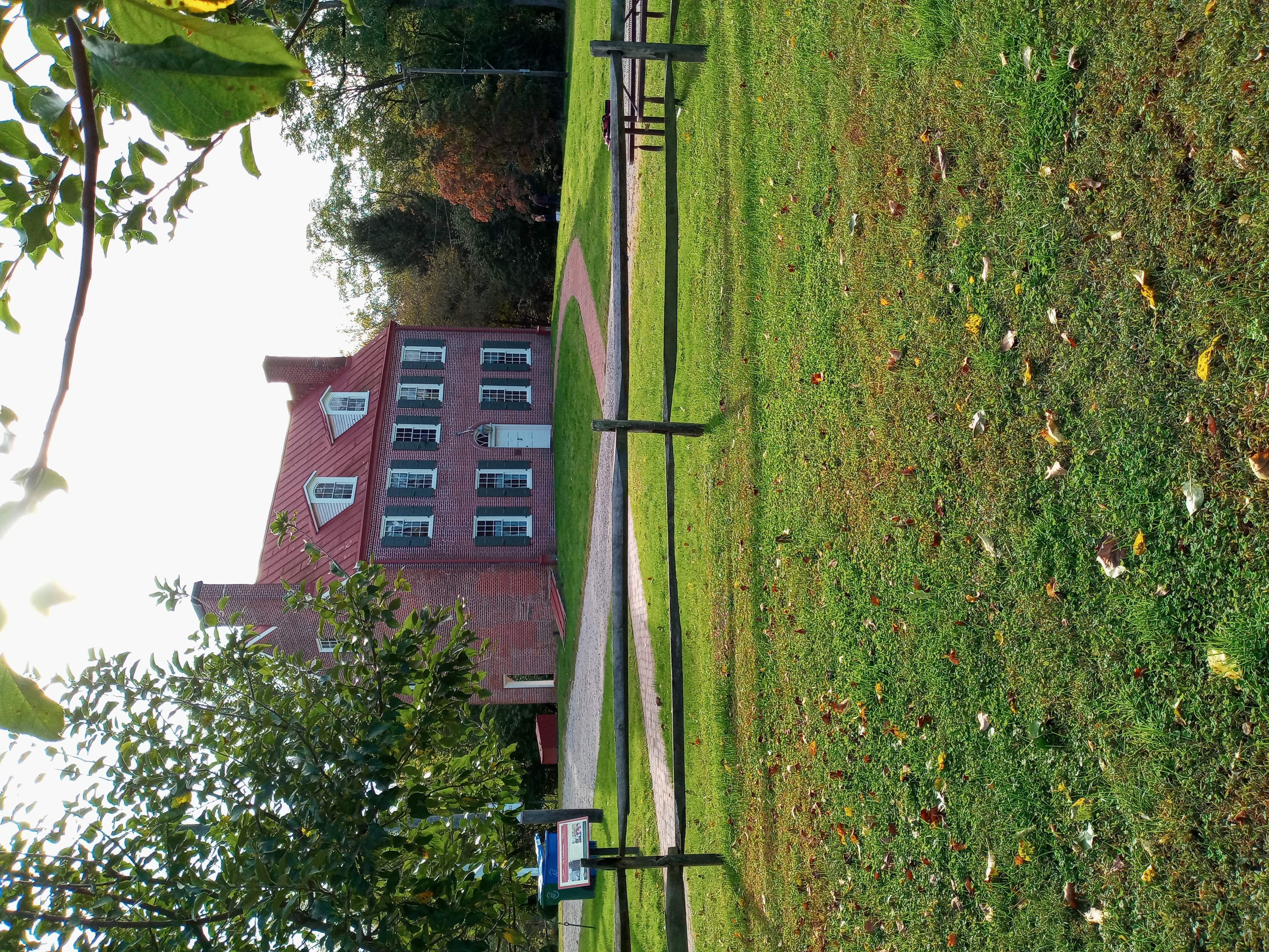 Two-story red brick colonial farmhouse with split-rail fence and autumn foliage.