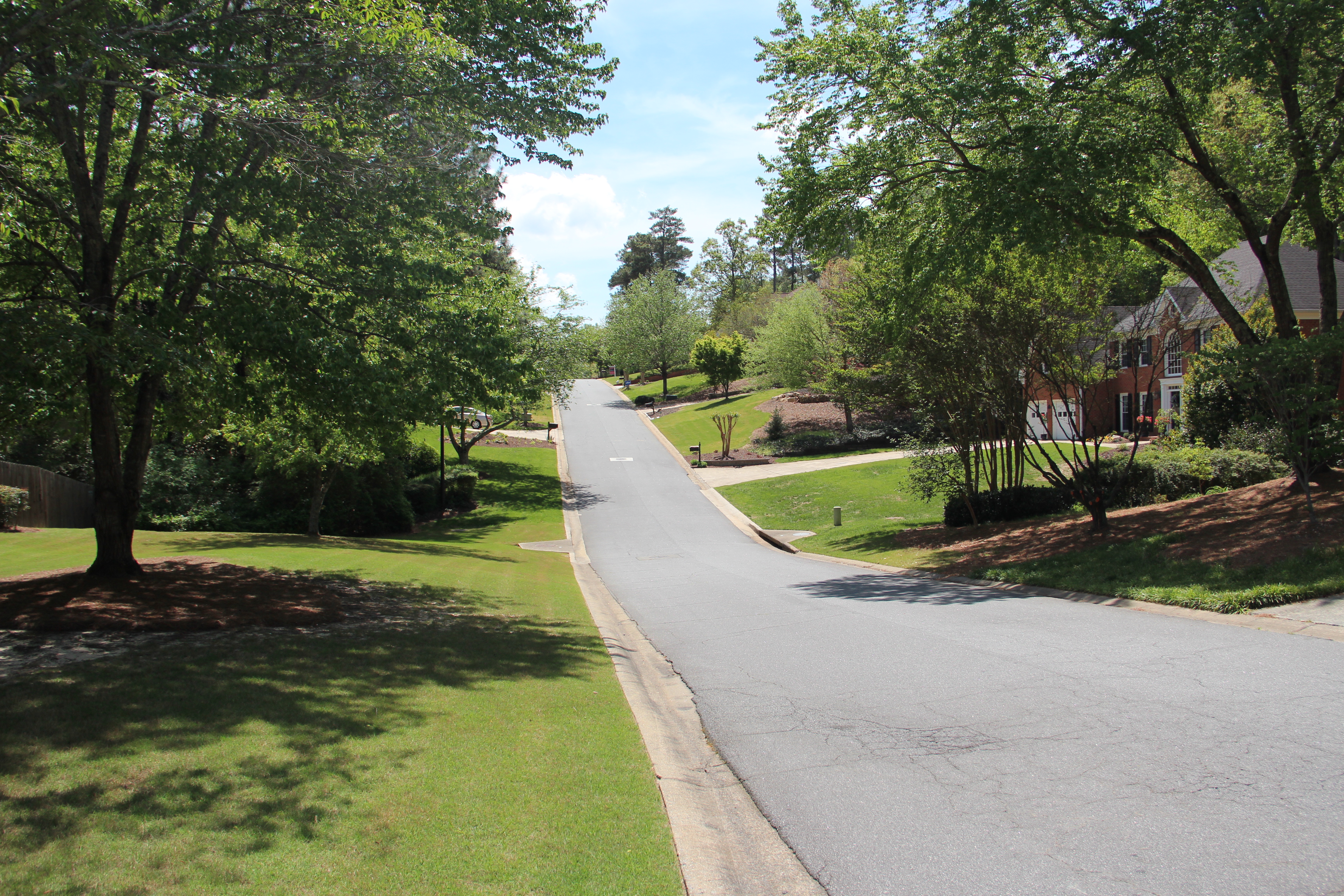 Tree-lined residential street with sidewalk and brick house in East Cobb, Georgia.
